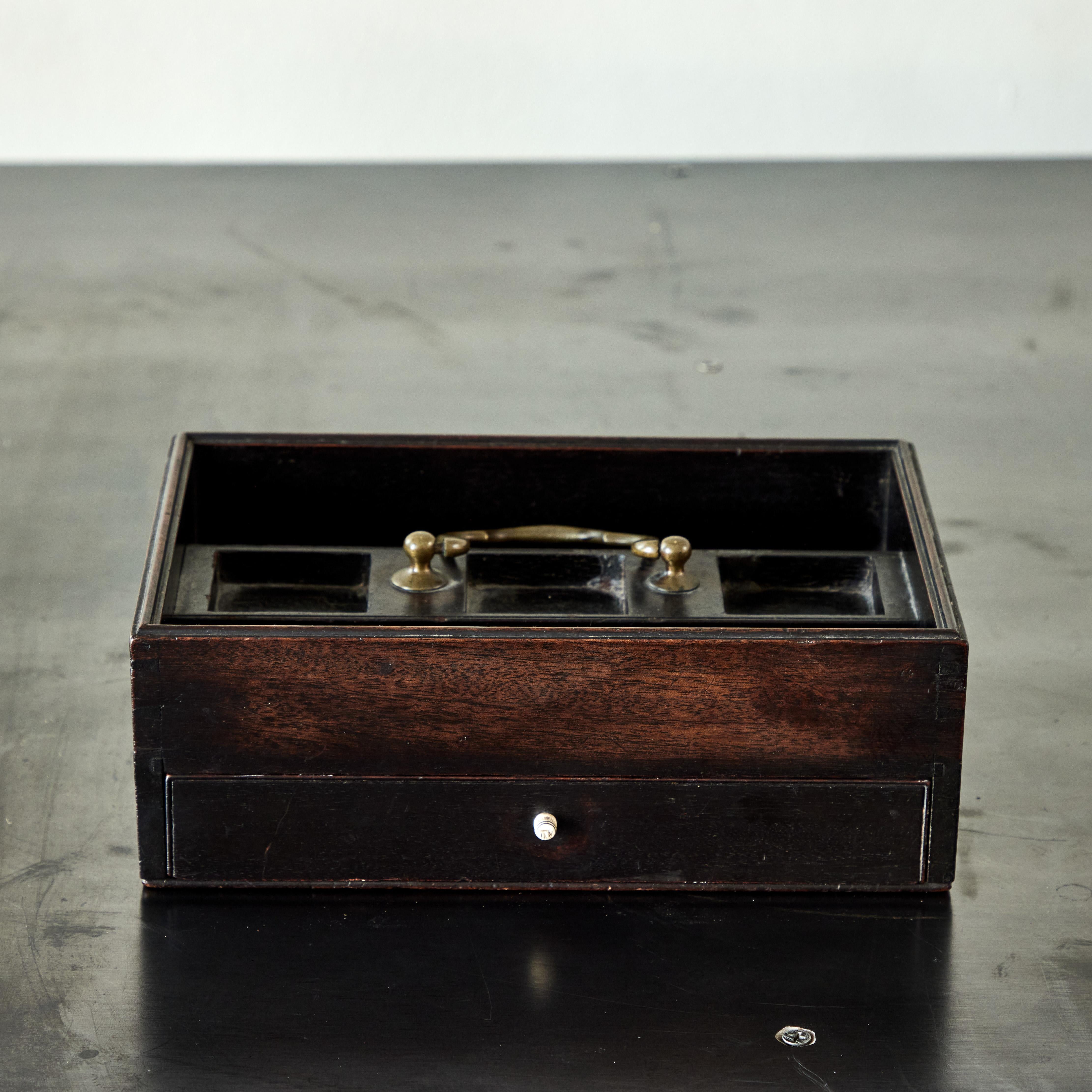English early 19th-century dark wooden desk box. Featuring a thin wide drawer with bead-shaped brass pull, four upper compartments of various sizes and a U-shaped brass handle. A handsome and discreet form of storage and decorative