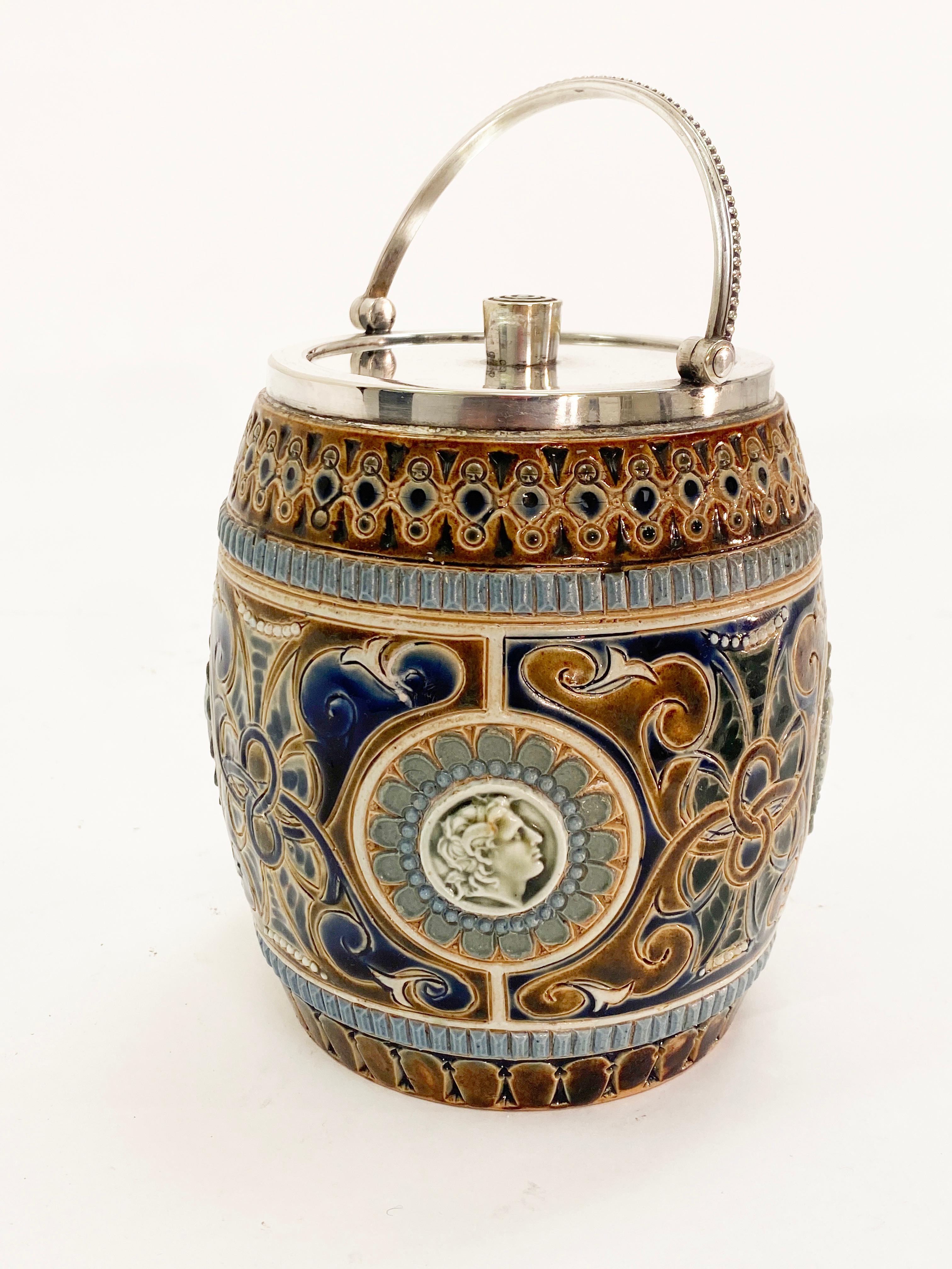 Beautifully crafted biscuit barrel with silver plate lid. Doulton Lambeth manufactured with ornate designs that cover the entire container. Grecian faces surrounding the structure of the barrel. 

19th century

Measures: Height 6”
Width