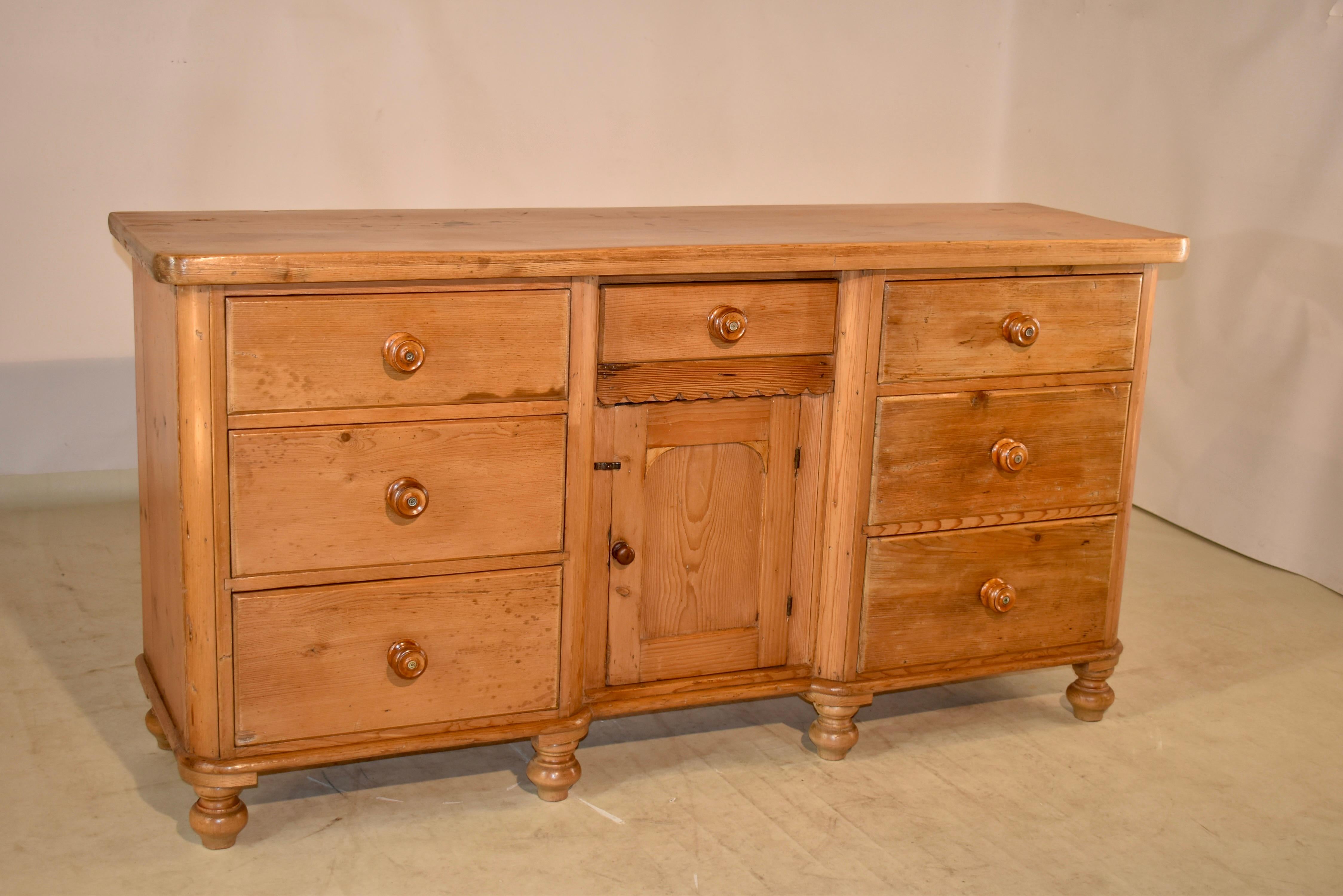 19th century pine dresser base from England with a two plank top, following down to simple sides. There are two banks of three drawers flanking a single drawer over a single door, which opens to reveal storage. The center is stepped back for added