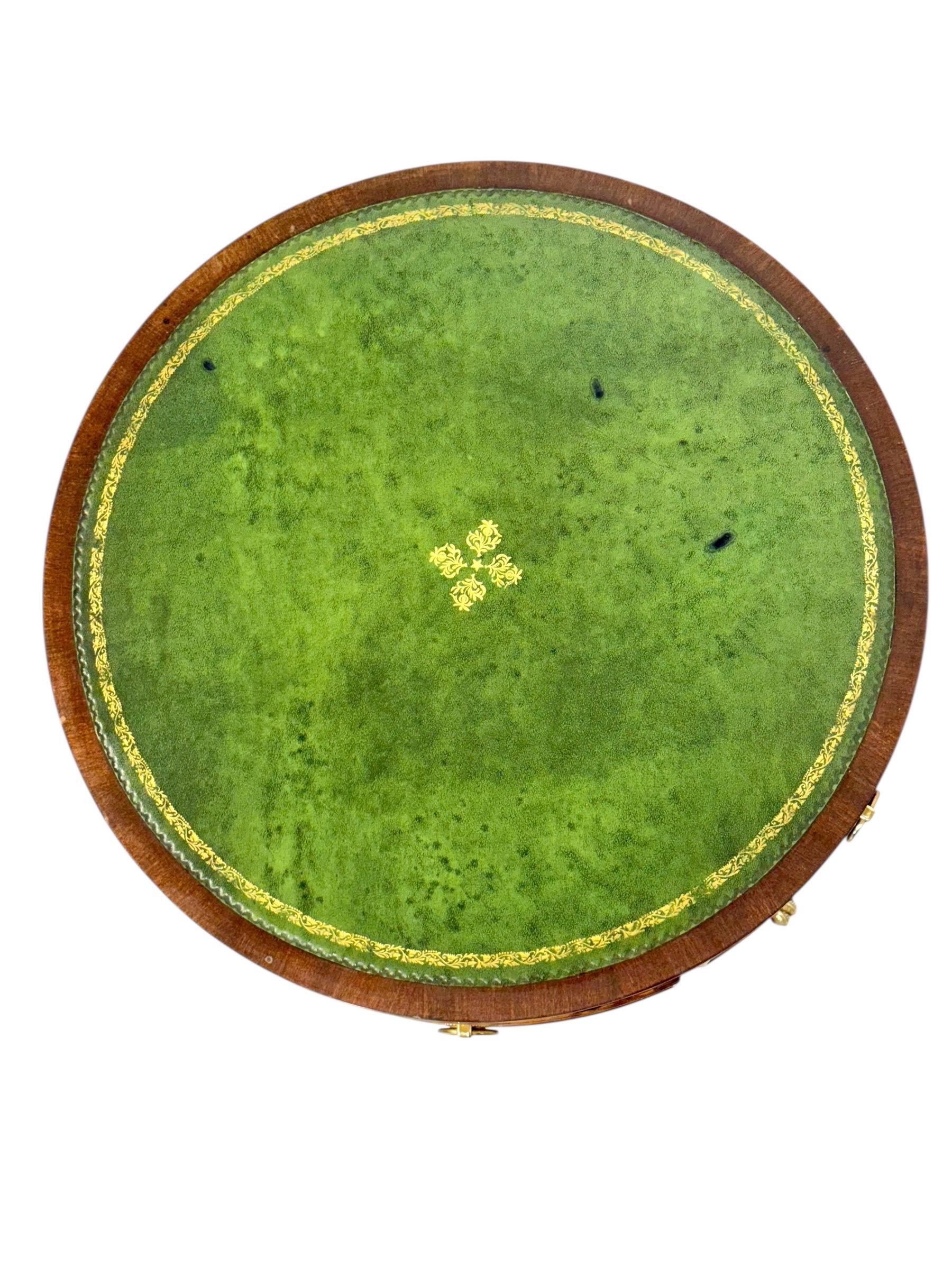 This elegant English drum gueridon, dating from the early 19th century, is crafted from finely polished walnut and reflects the refined taste of the Regency period. The circular top is inset with a richly colored green gilt-tooled leather surface,