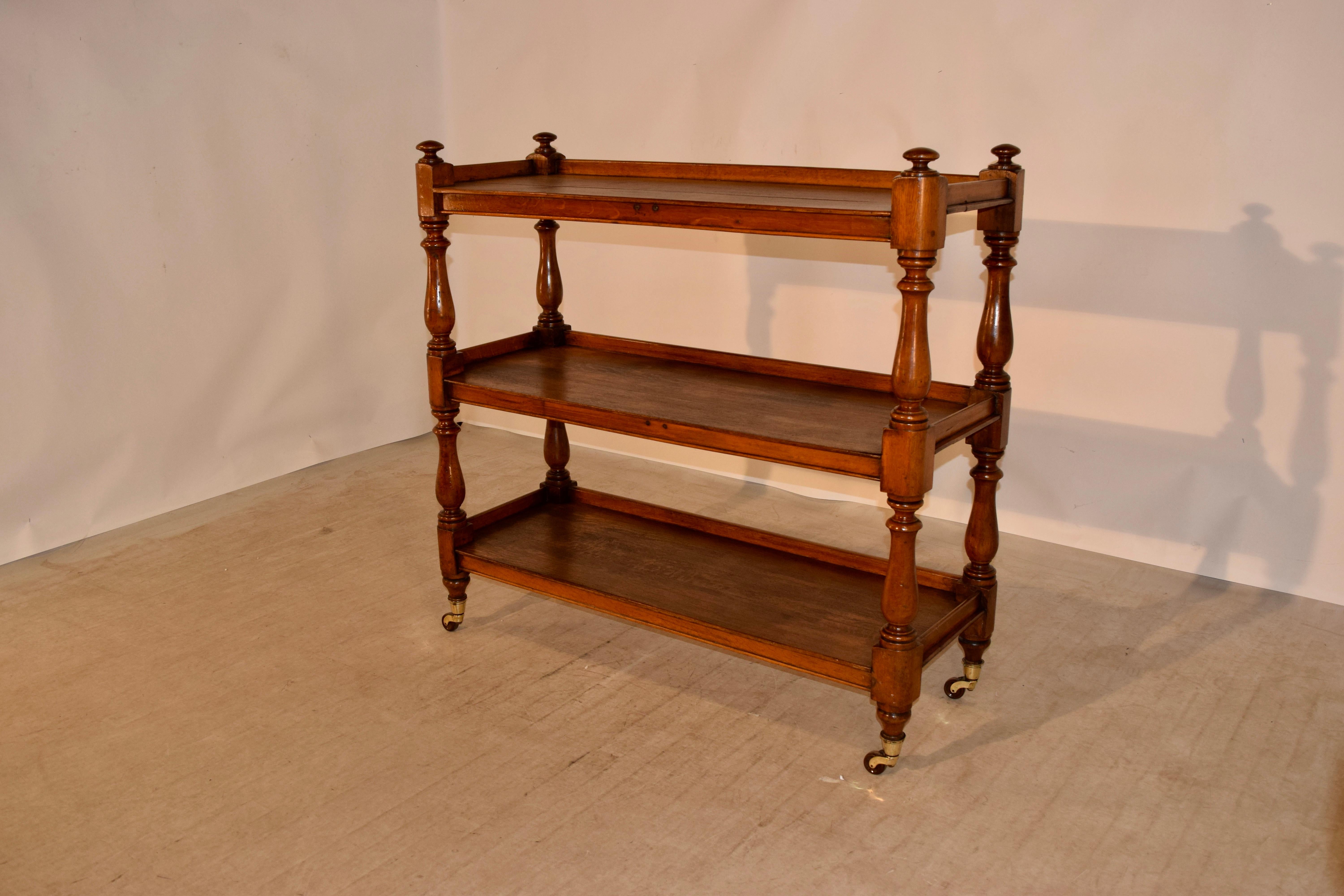 19th century oak dumbwaiter from England with three shelves, all with galleries and hand turned shelf supports. Supported on original brass casters. Staining on shelves due to age and use.