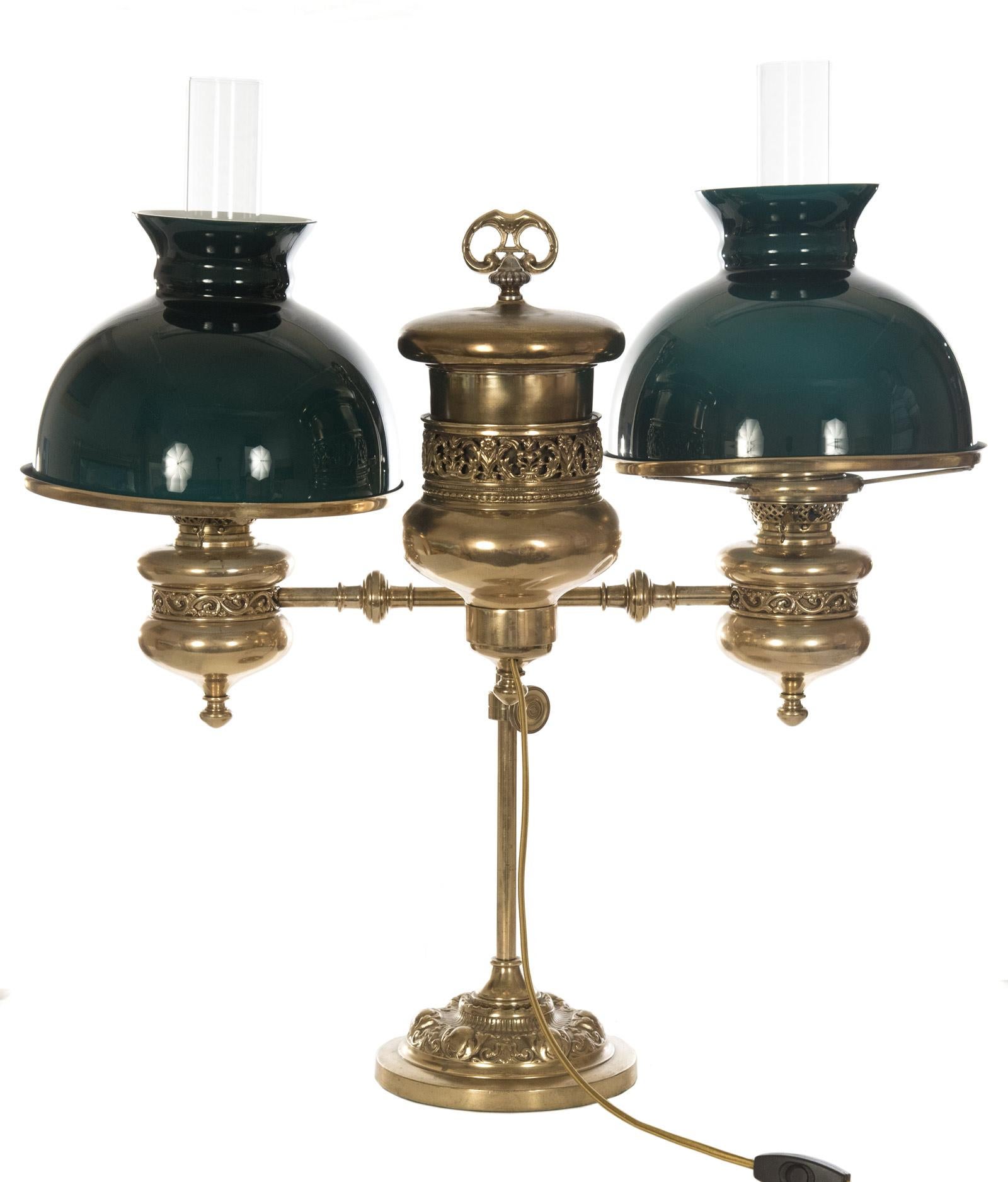 An electrified, late 19th century double student gas lamp with green case glass shades raised on finely chased and pierced brass fuel reservoirs, the arms affixed to an adjustable central stem, all raised on a domed base. Marked on light knobs 