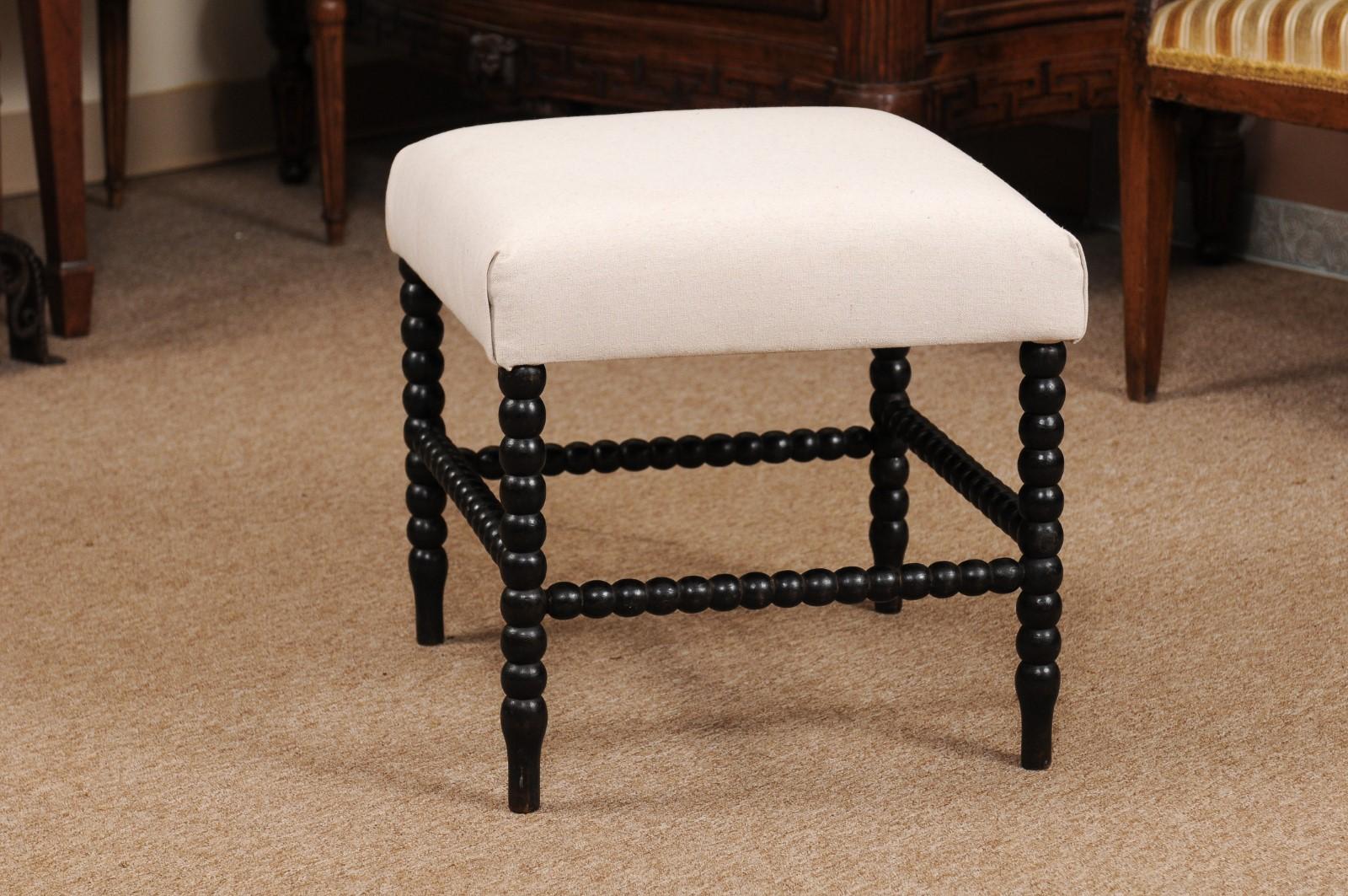 The 19th century English ebonized bobbin turned stool/bench with linen upholstered seat with box stretcher.