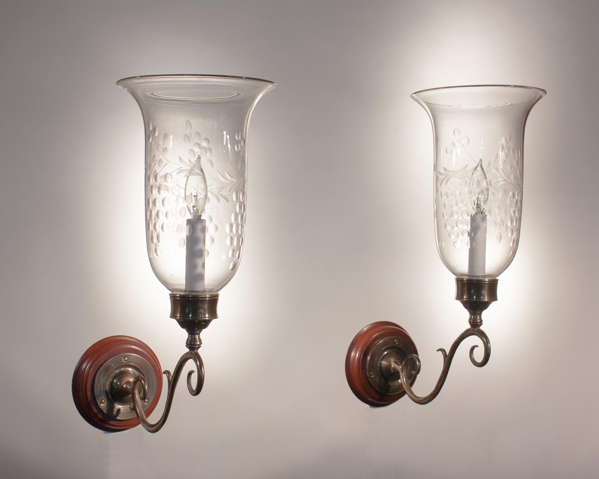 Pair of English hurricane sconce shades with a lovely flared form and an etched grape and vine motif. These circa 1870 shades have very faint fogginess in spots, which is not uncommon in hand blown glass of this age. There is also a small chip on