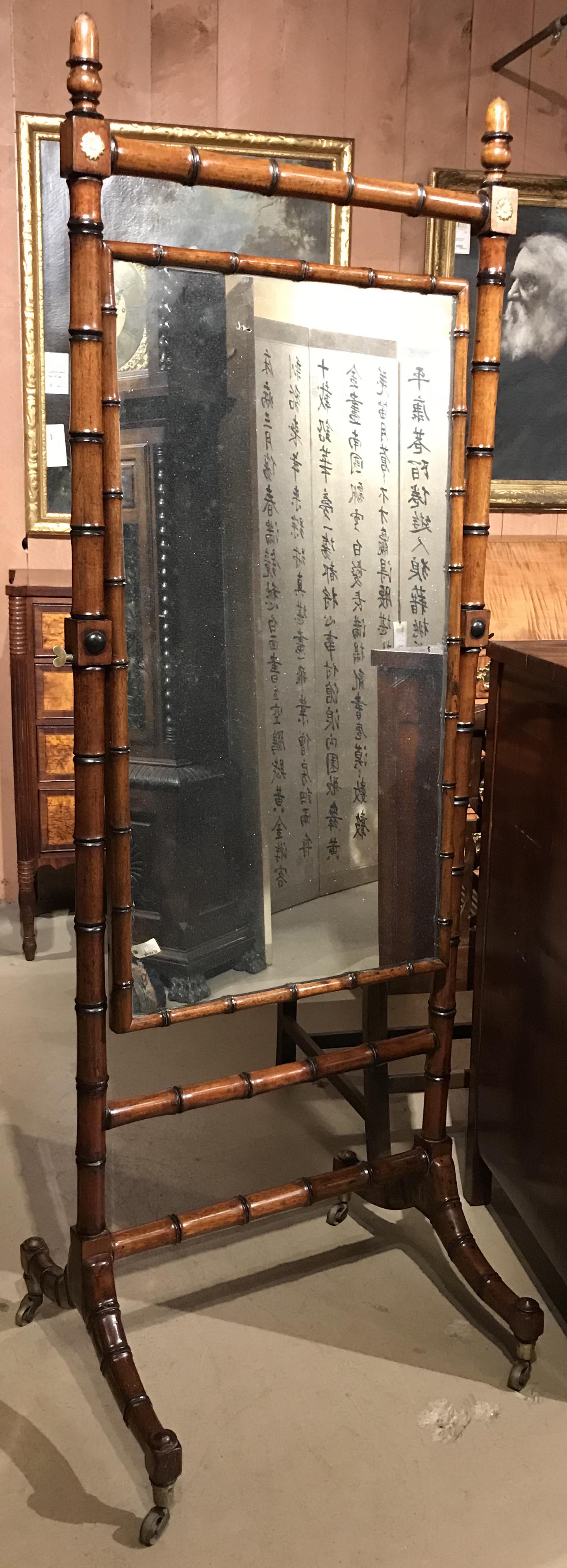 A fine example of a faux bamboo border rectangular cheval mirror on stand, with gilt carved upper corner rosettes, and brass casters on its base frame. Very good overall condition, with some old repairs, mirror surface losses, other minor