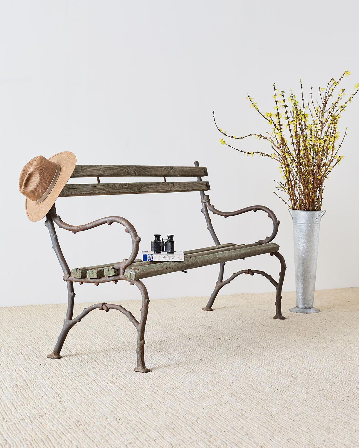 Rustic 19th century English garden bench having a branch twig style faux bois frame made of cast iron. The bench has graceful curved arms and legs with beautiful distressed patina on the cast iron and wood slats. Lovely understated style with a