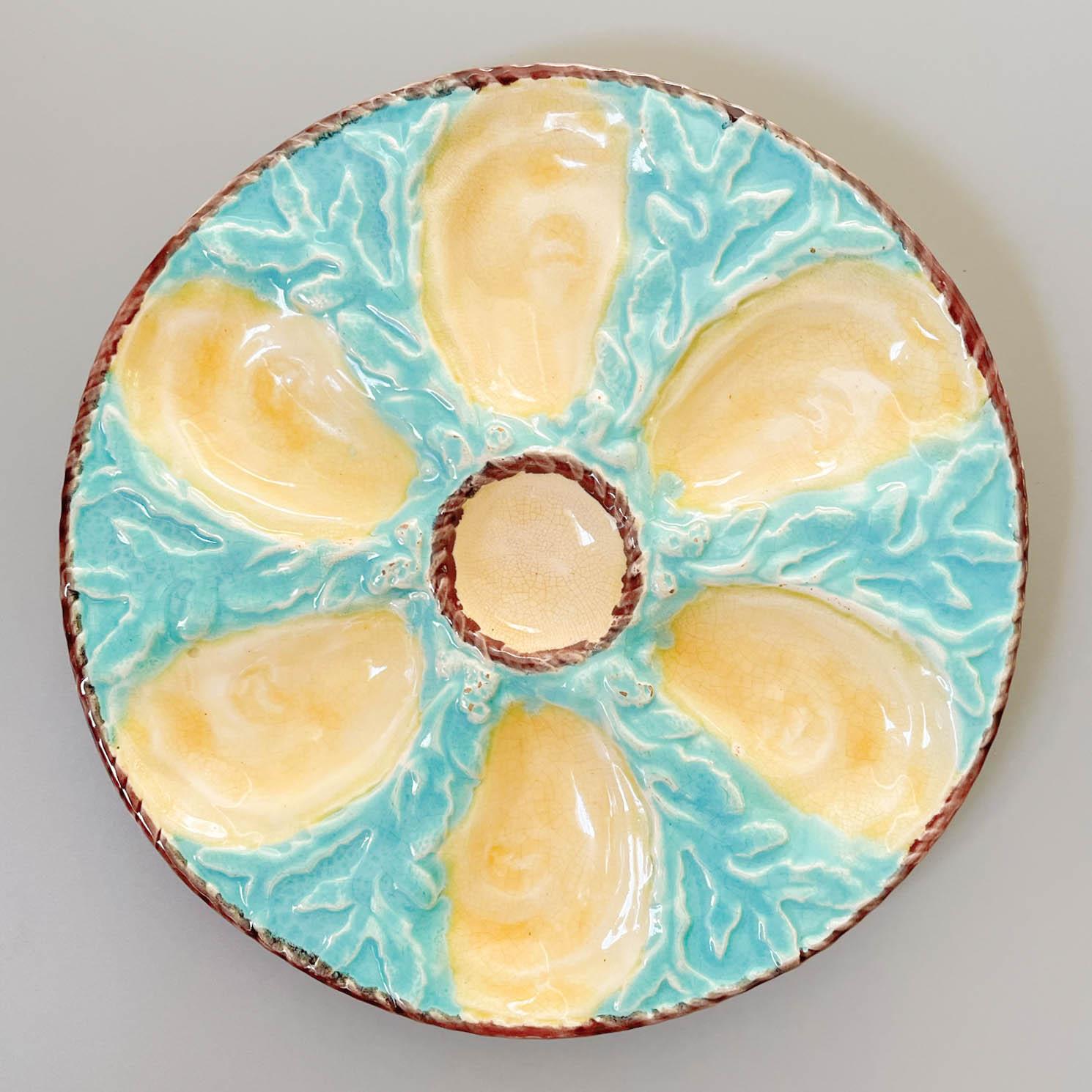 A 19th Century English glazed majolica oyster plate with six cream oyster wells surrounding a center well for sauce and with light turquoise blue ground with seaweed relief. A light brown nautical rope border encircles the center well and the outer