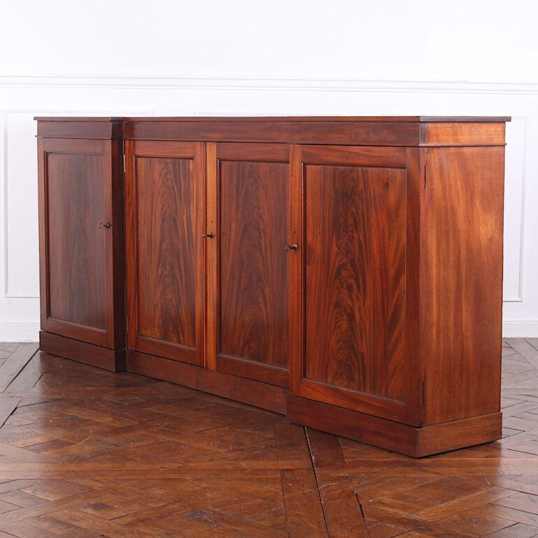 An English reverse-breakfront four-door side cabinet or buffet, the doors with dramatic flame mahogany panels. A bank of interior drawers is fitted in one section; the other three sections have shelves, circa 1830-1840.

  