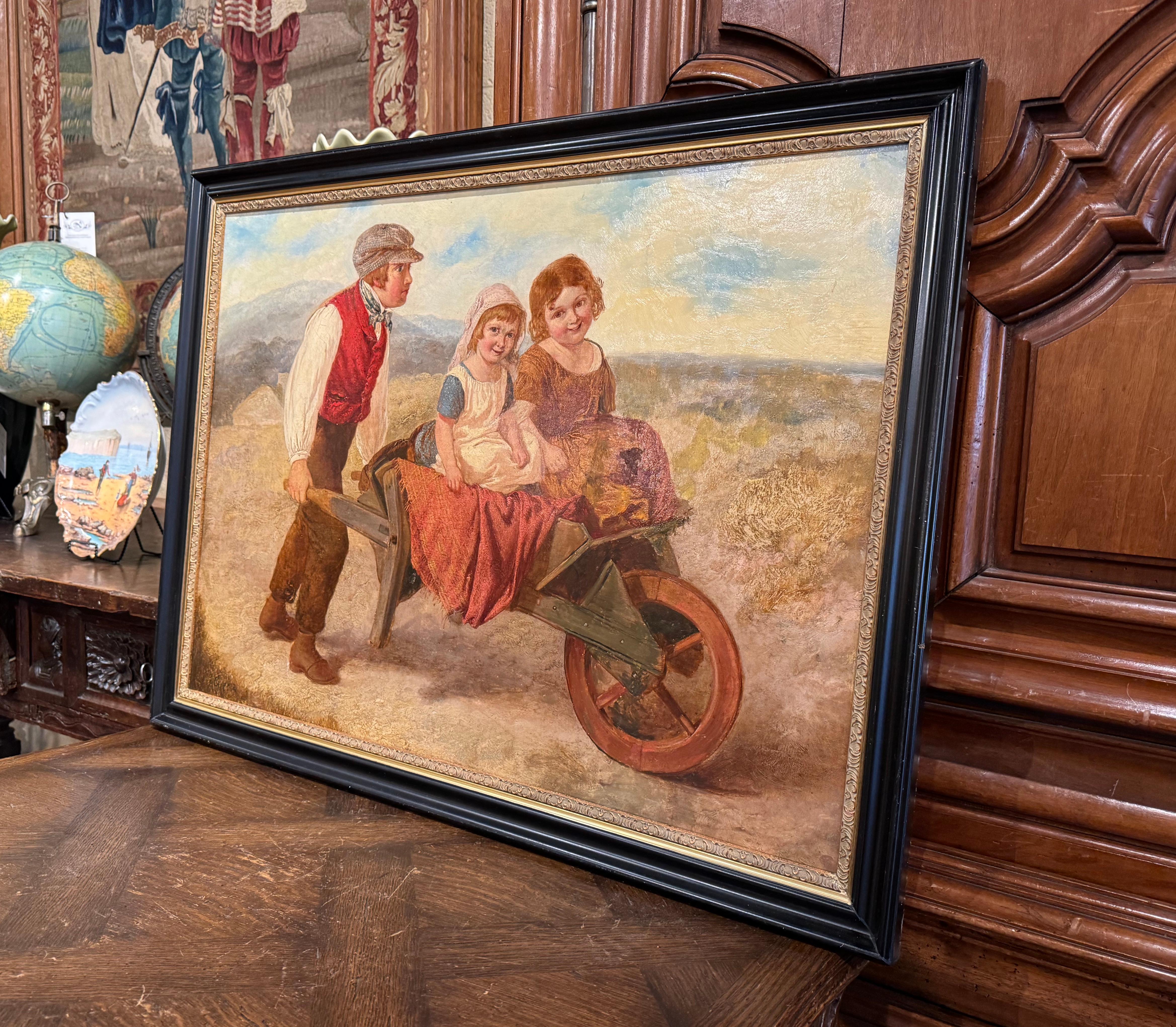 Decorate a den or a bedroom with this elegant antique painting. Created in England, circa 1860, and set in blackened and gilt wood frame, the canvas depicts three children in the countryside riding in a wheelbarrow. The bucolic piece has a wonderful