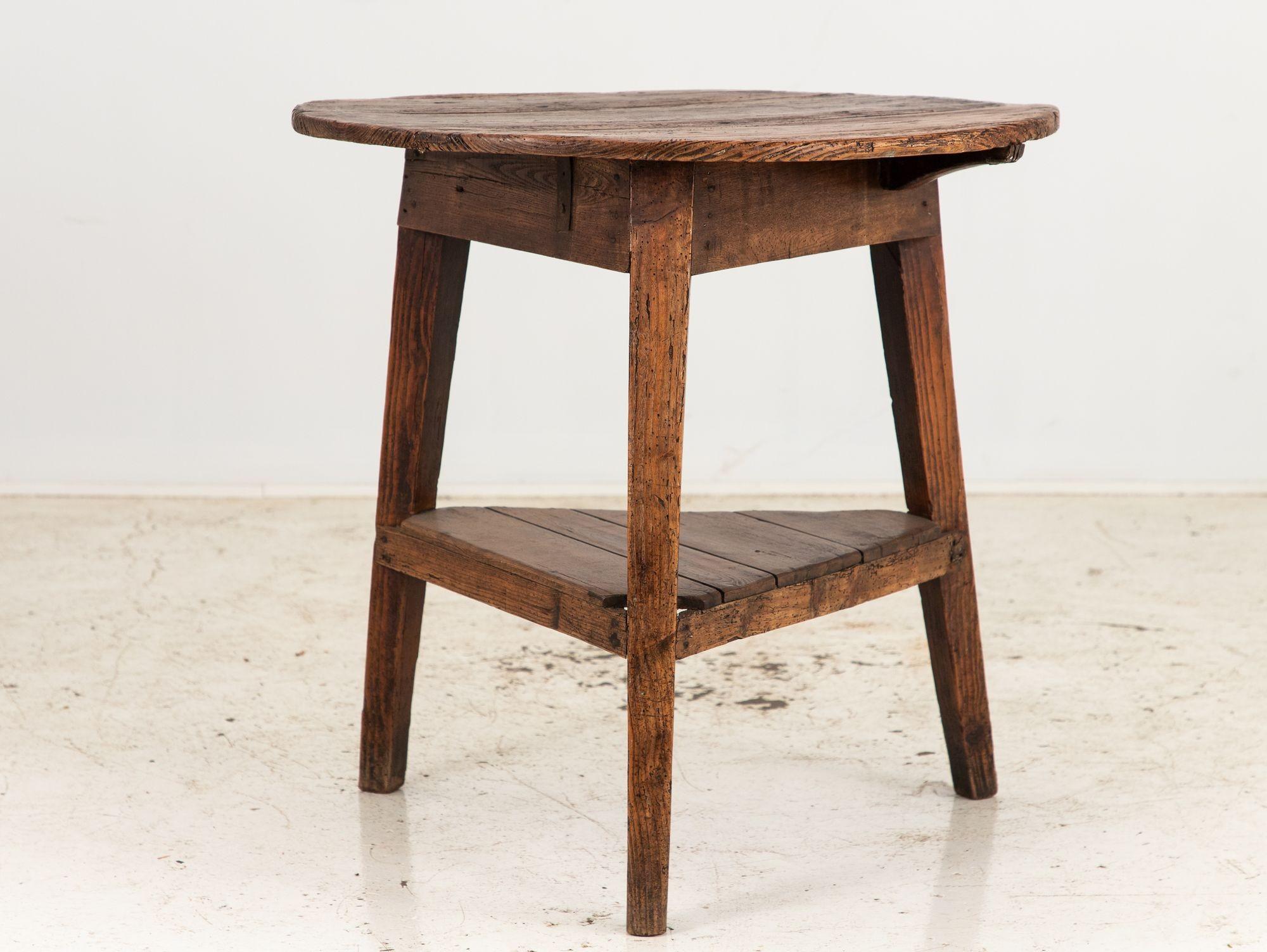 Cette charmante table de cricket ou de pub anglaise en bois fruitier du XIXe siècle dégage un charme antique. Son plateau rond est soutenu par trois pieds robustes avec une étagère inférieure, incarnant le style emblématique des pubs anglais.