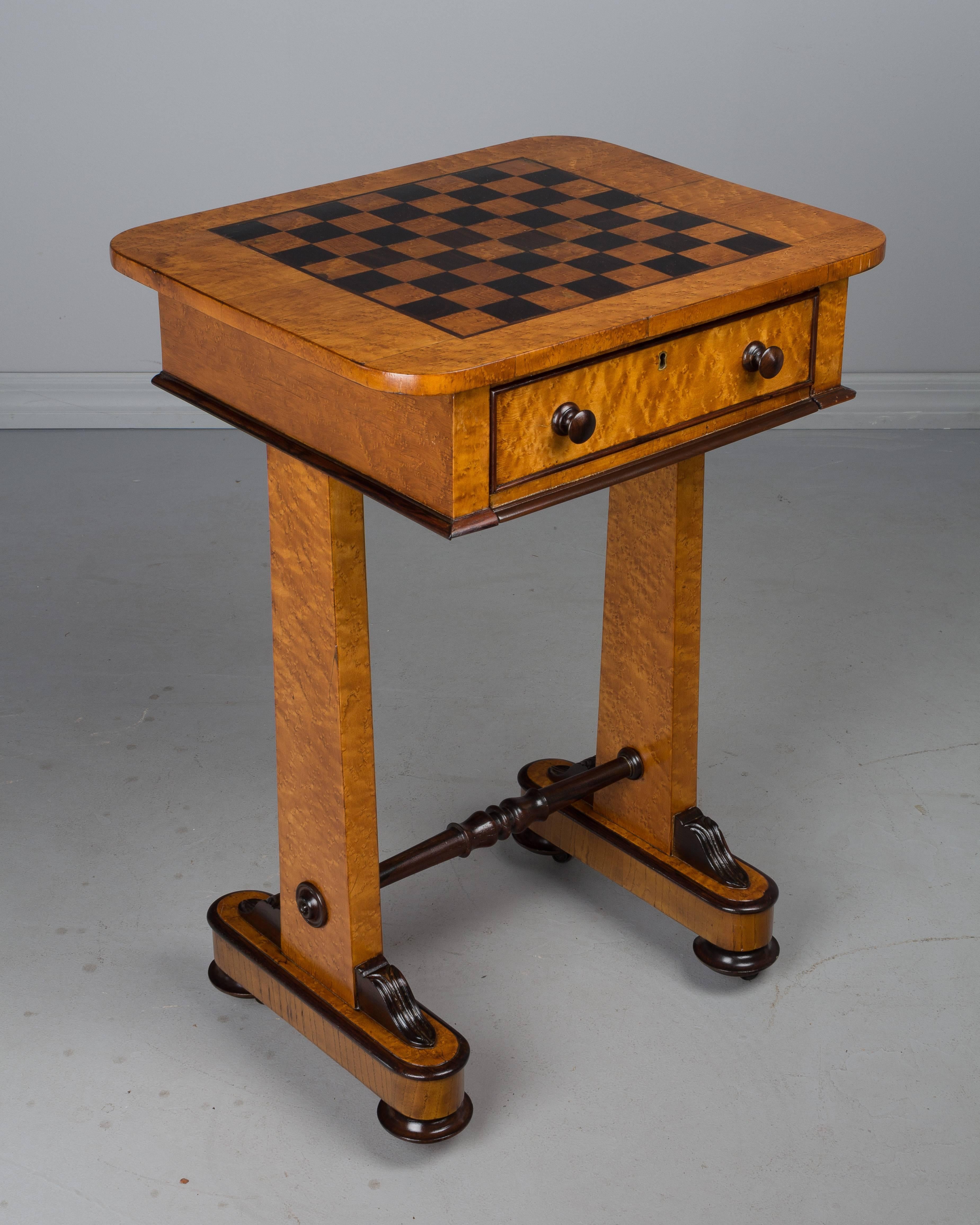 An 19th century English game table made of bird's-eye maple and rosewood with marquetry checkerboard playing surface. Finely crafted with a single dovetailed drawer and pull-out shelf, each lined with cream suede. Lock is present but there is no