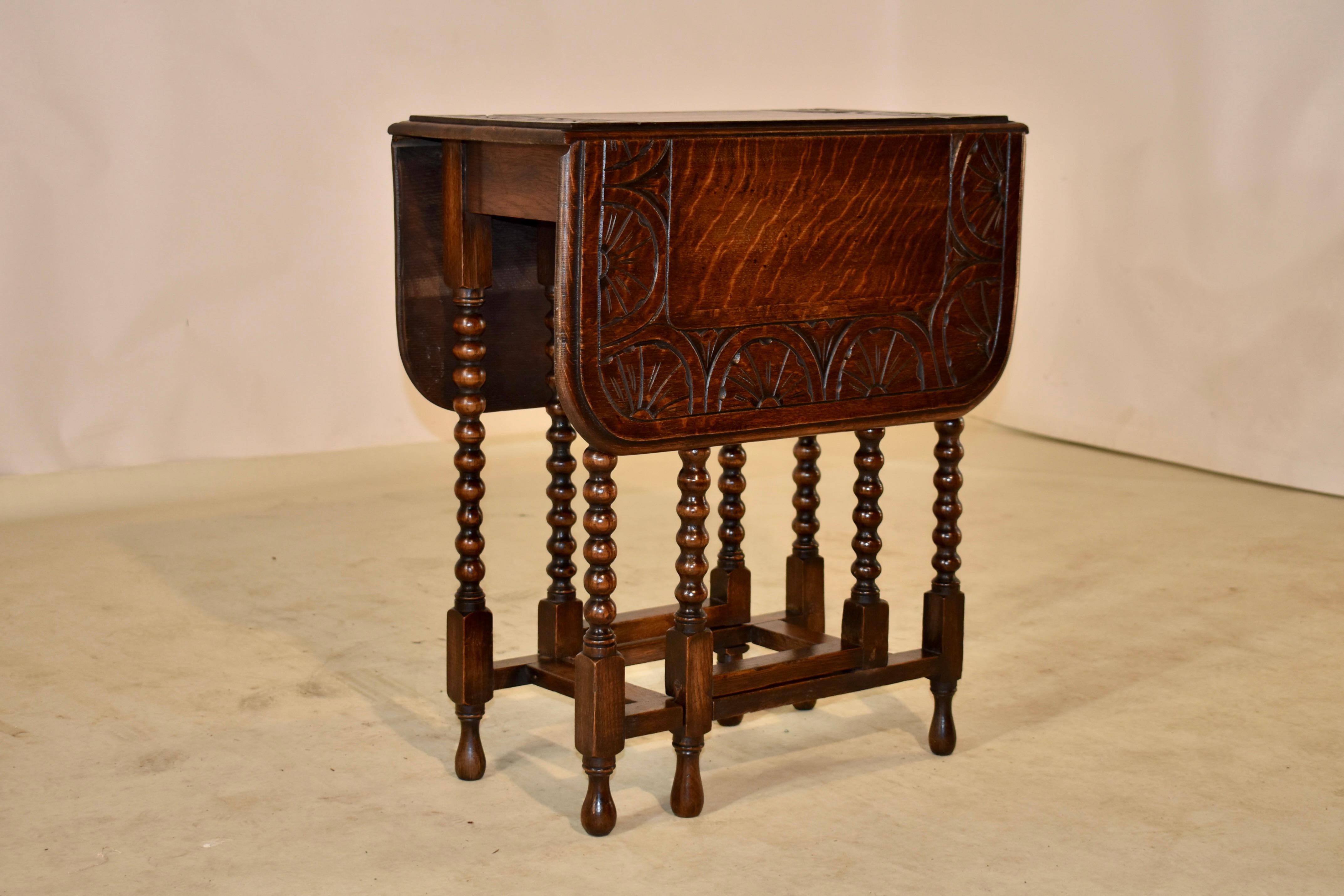 19th century oak gate leg table from England with hand carved decorated banding around the top, also with a beveled edge. The top follows down to simple aprons and the table is supported on hand turned bobbin legs. The legs and gates are joined by