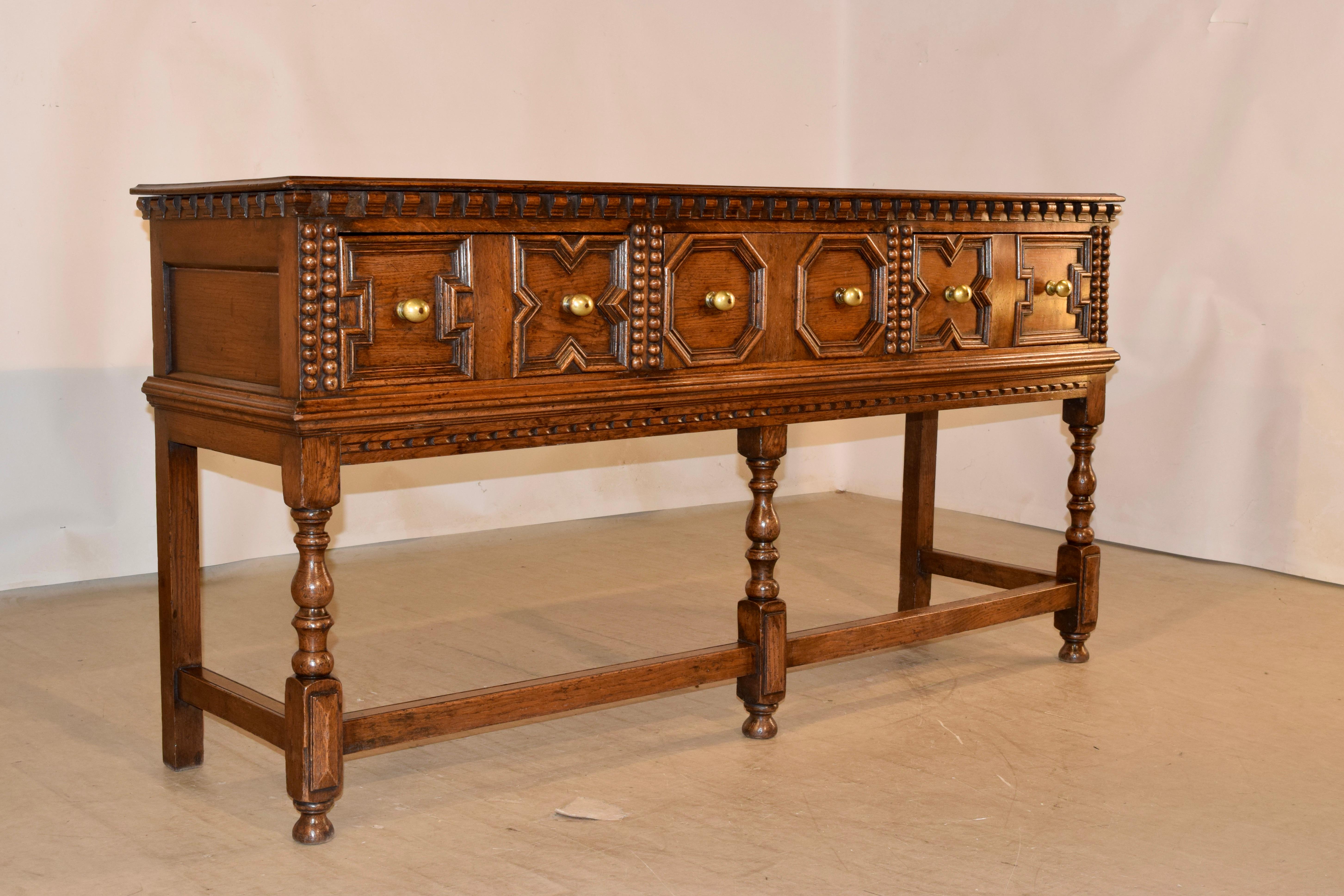 19th Century oak geometric sideboard from England. The top is made from a single board, and has a beveled edge, following down to wonderfully detailed applied corbel moldings on the case and paneled sides. There are three drawers in the front, all