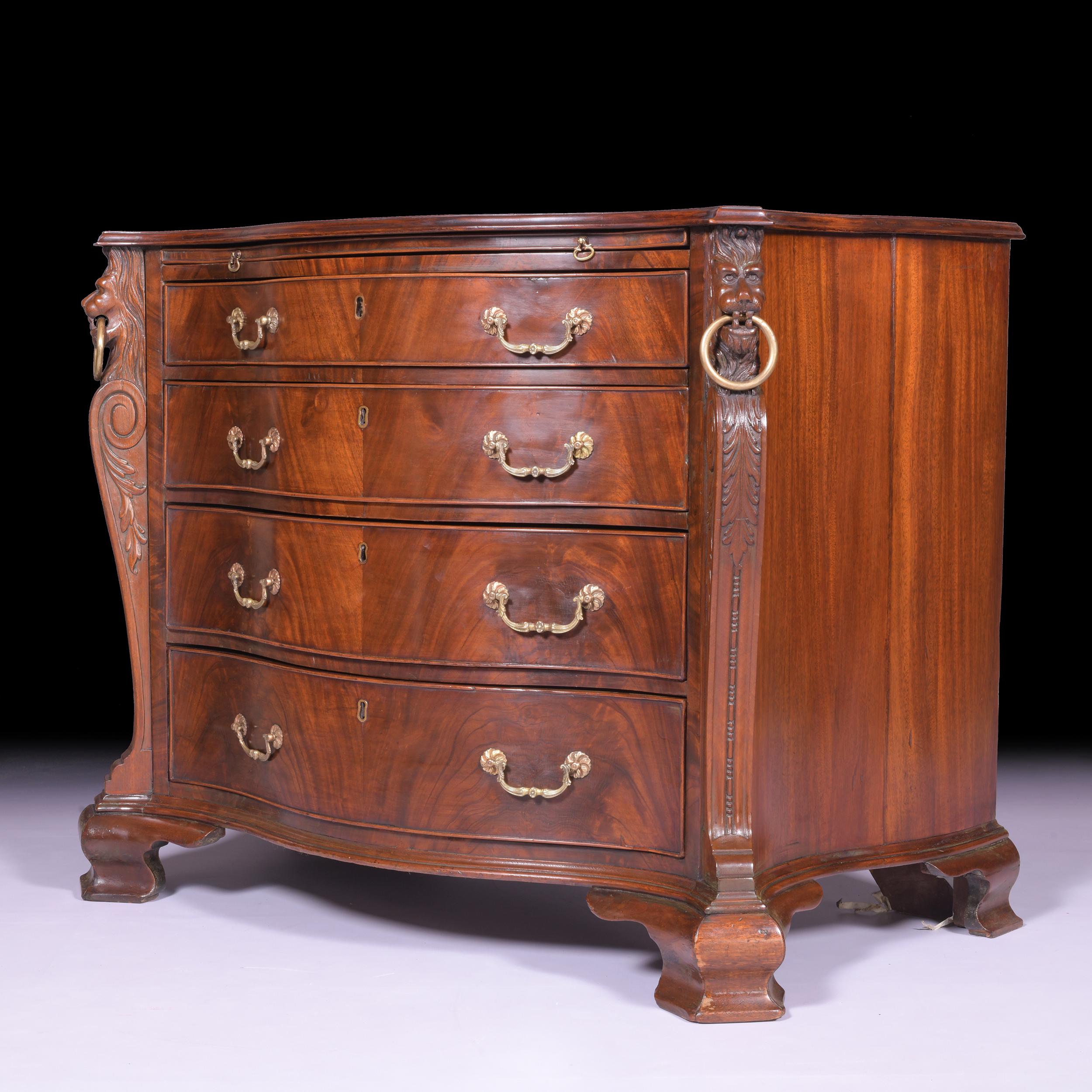 A superb George II style mahogany serpentine shaped commode in the style of Thomas Chippendale, with a moulded serpentine top above a slide and four long graduated drawers between scroll and mask head stiles, on ogee bracket feet.

Circa