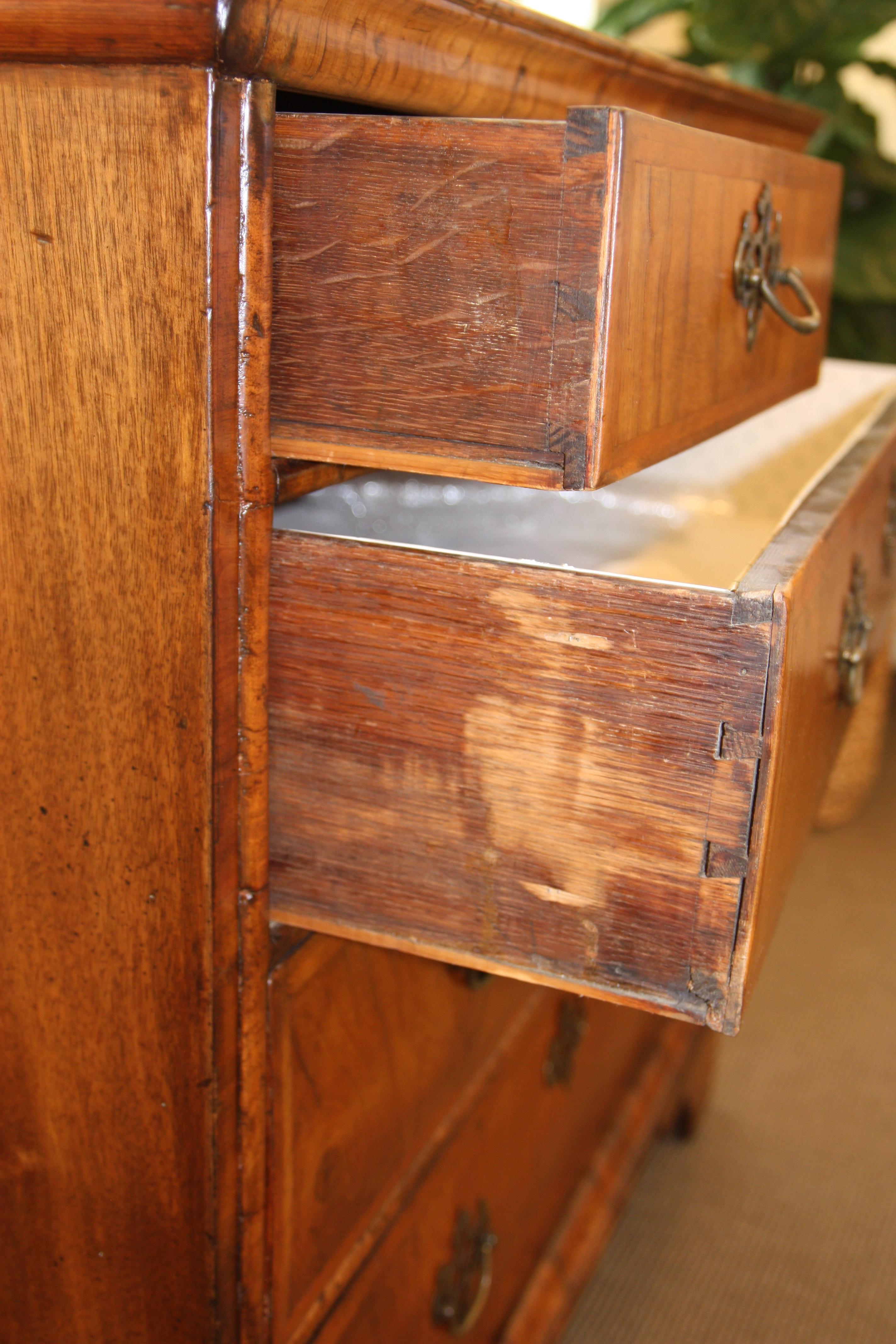 This 19th century English George III commode features a rectangular top with inlay sitting above two small drawers. The smaller drawers sit above three larger graduated drawers making up the rest of the facade. Each of the drawers is adorned with an