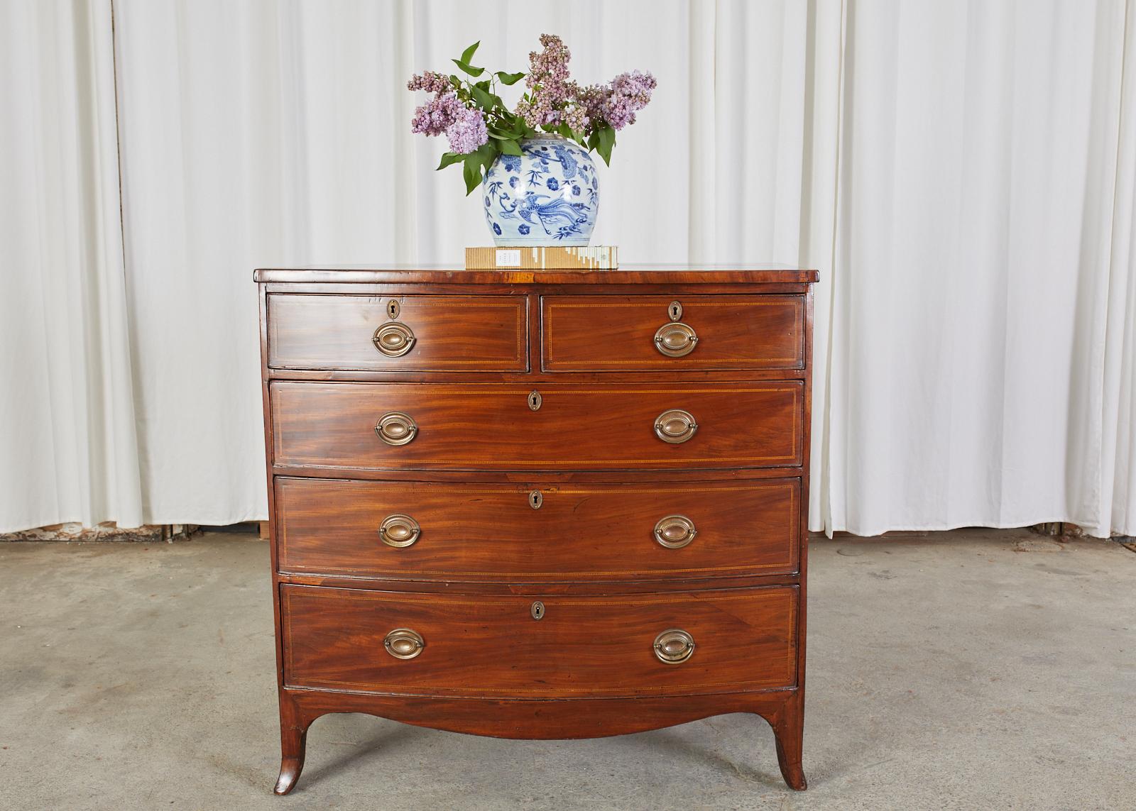Handsome 19th century mahogany bow front chest of drawers made in the English Georgian taste. The large case features five storage drawers with brass pulls. The drawers and case top are embellished with delicate thread inlay around the borders. The