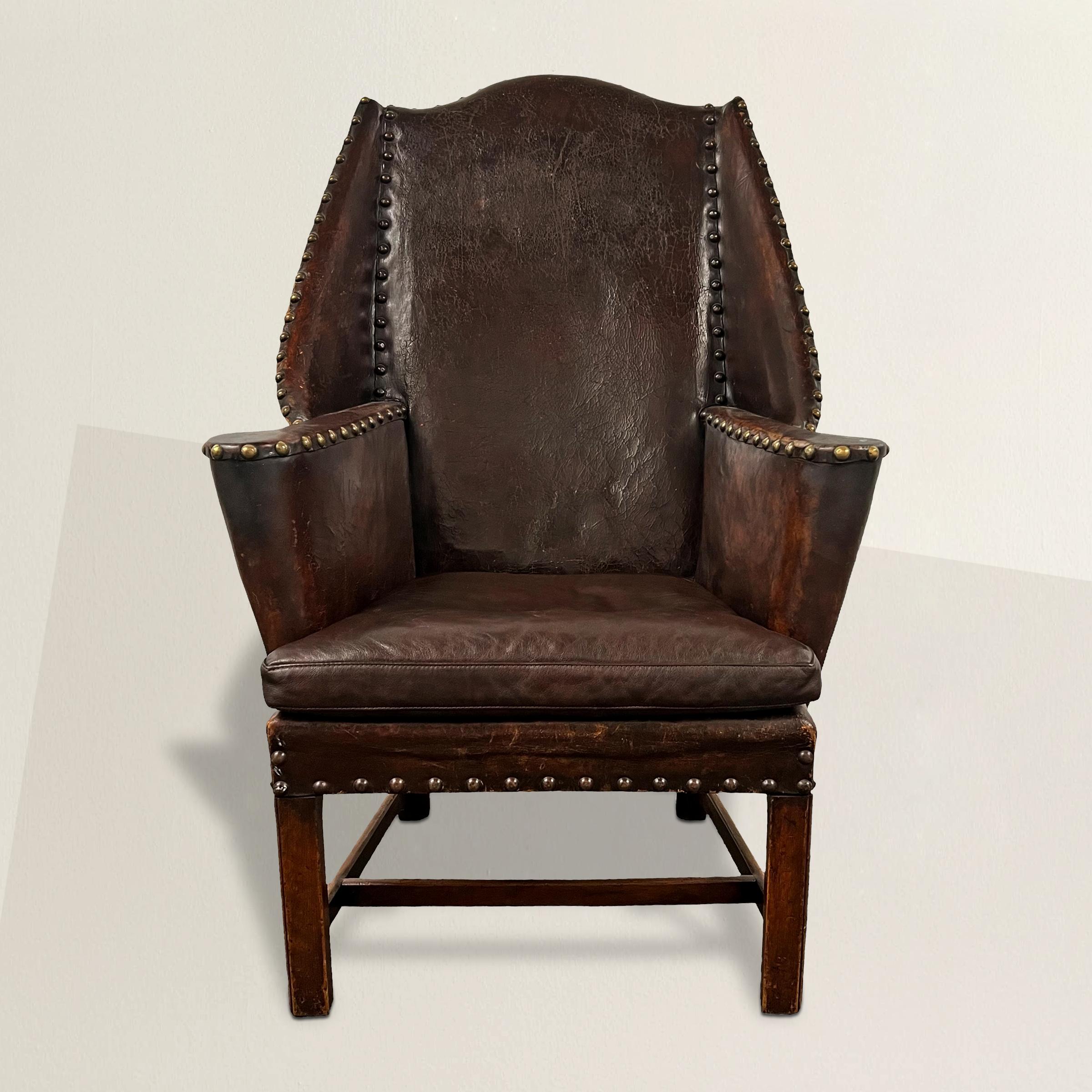 Embrace the refined elegance of 19th-century English design with this exquisite Georgian-style leather wing chair. Its intriguing flared wings, tapering down to meet out-turned arms, evoke a sense of timeless sophistication. Upholstered in its