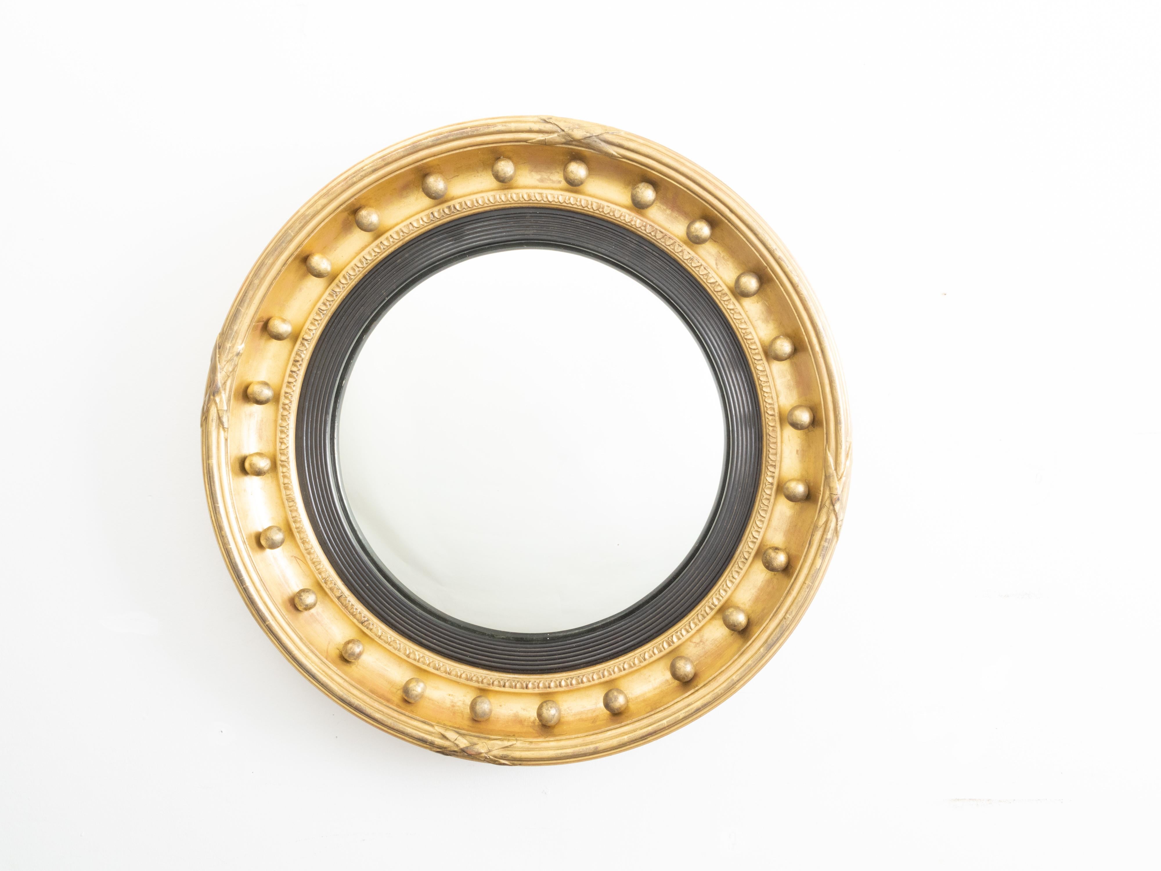 An English giltwood bullseye convex girandole mirror from the 19th century with ebonized reeded accents. Created in England during the 19th century, this circular mirror features a convex mirror plate, surrounded by a reeded molding of ebonized