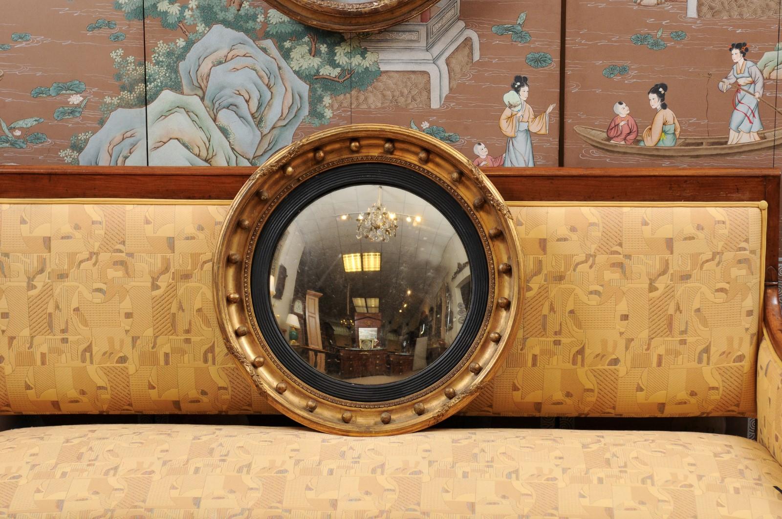 A 19th century English giltwood bull’s-eye mirror with convex glass, ebonized and round balls detail.