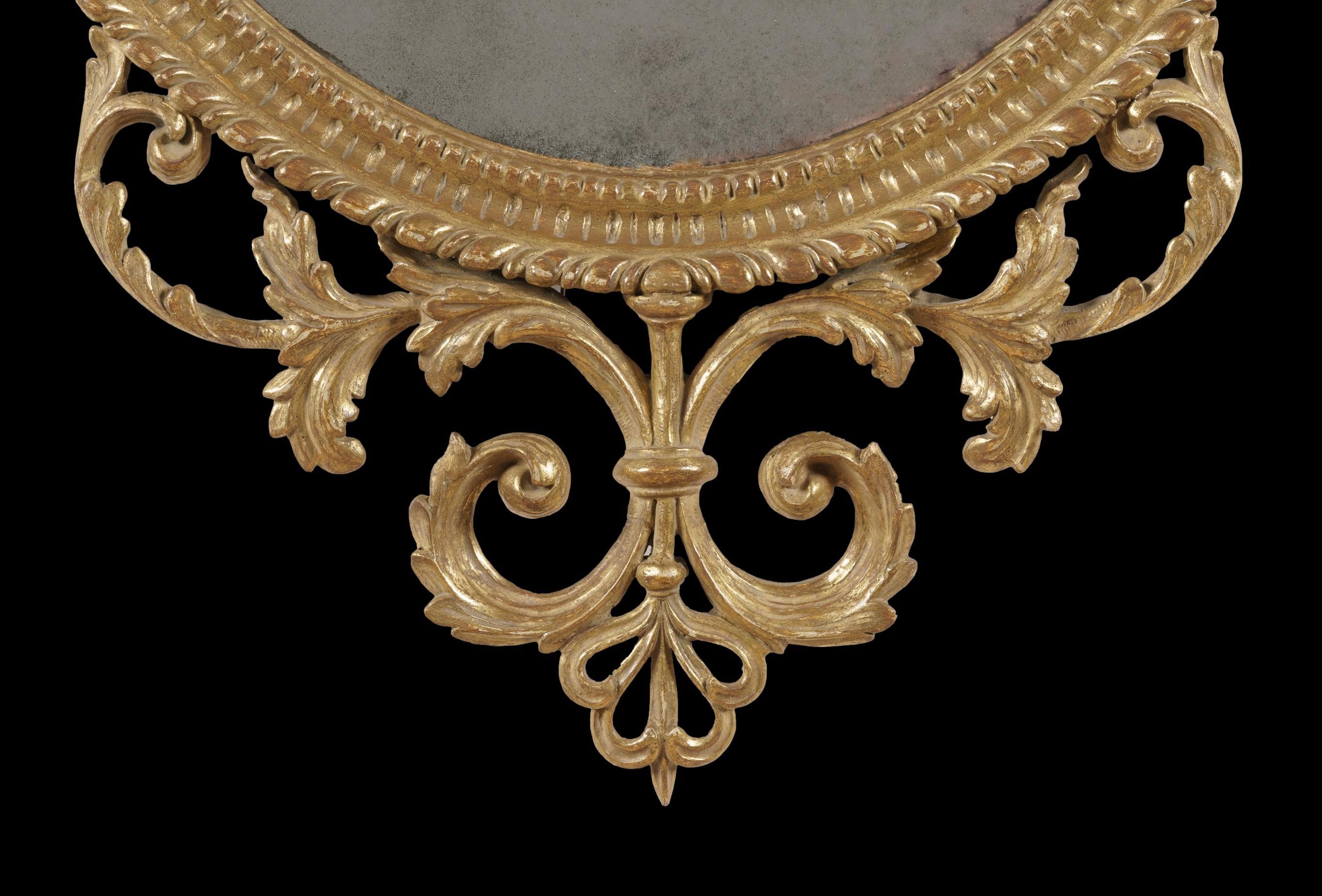 A fine mirror in the George III manner

Constructed from giltwood, housing an oval mirror plate within a carved moulding, the top and base issuing scrolling acanthus leaves, a central vase motif above with draped bellflower husks adorning the