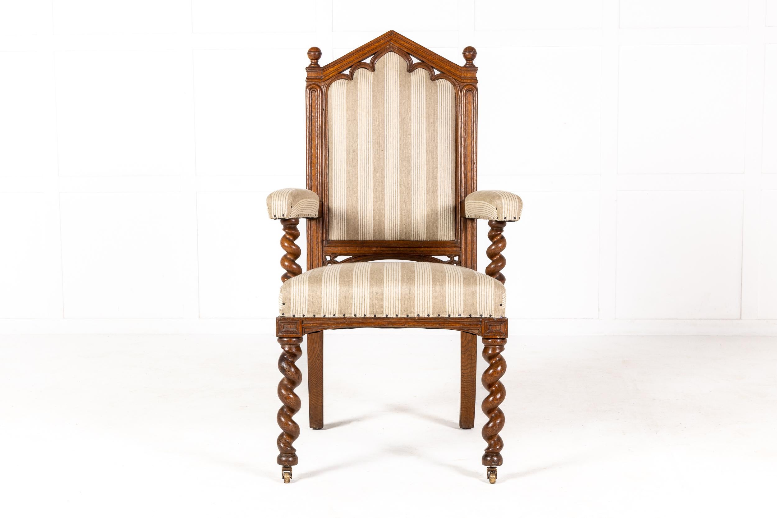 19th century English oak gothic armchair carved in solid oak. Having a typically angled, pointed arch over its high back with traditional gothic arches and finials. Good deep proportions having a padded back with inset and padded armrests with