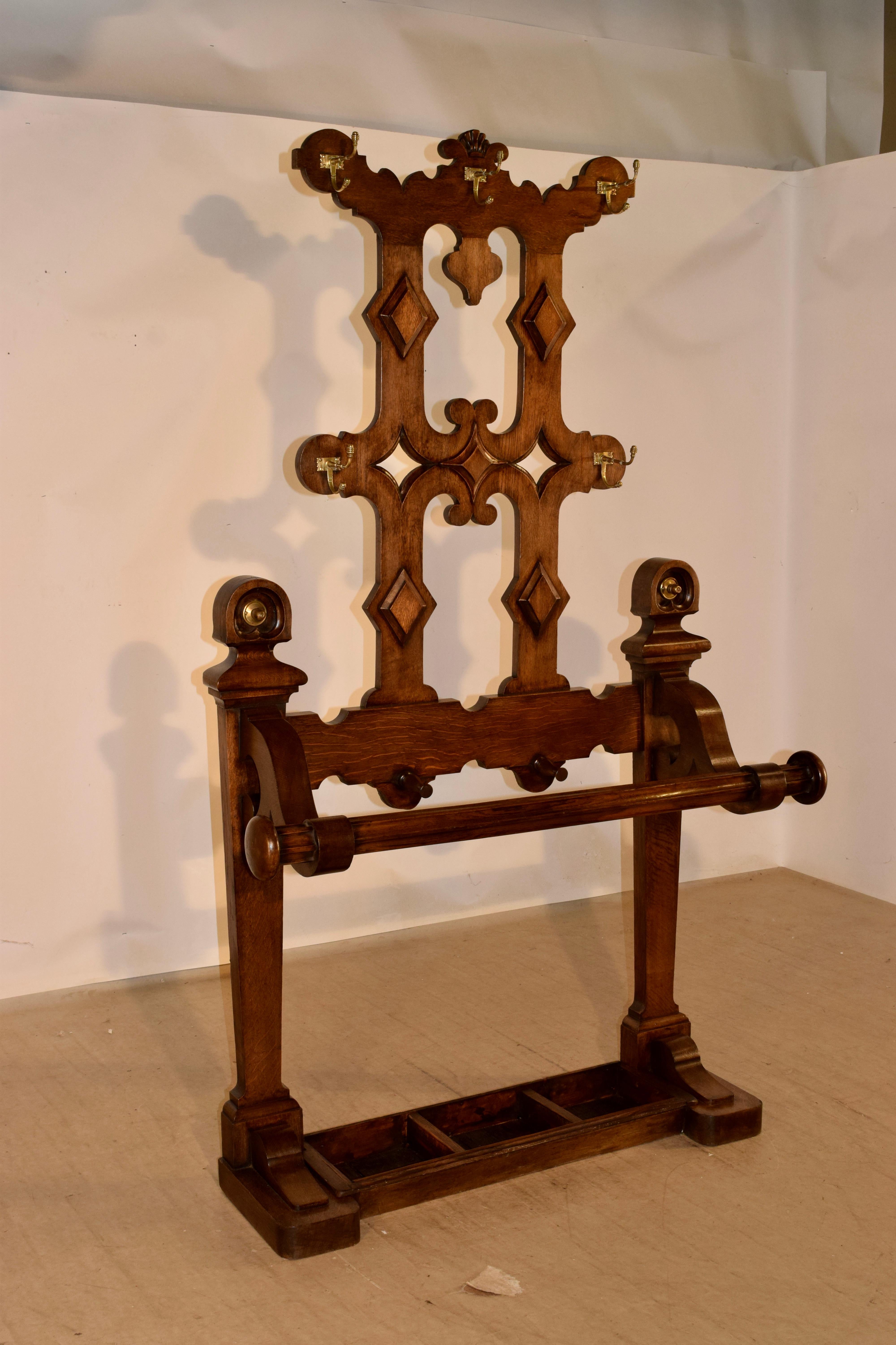 19th century English hall stand made from oak. It is a lovely scalloped and shaped piece with five hooks for coats or hats and has a large umbrella or cane stand at the base. there are two additional hooks at the bottom for umbrella or cane handles.