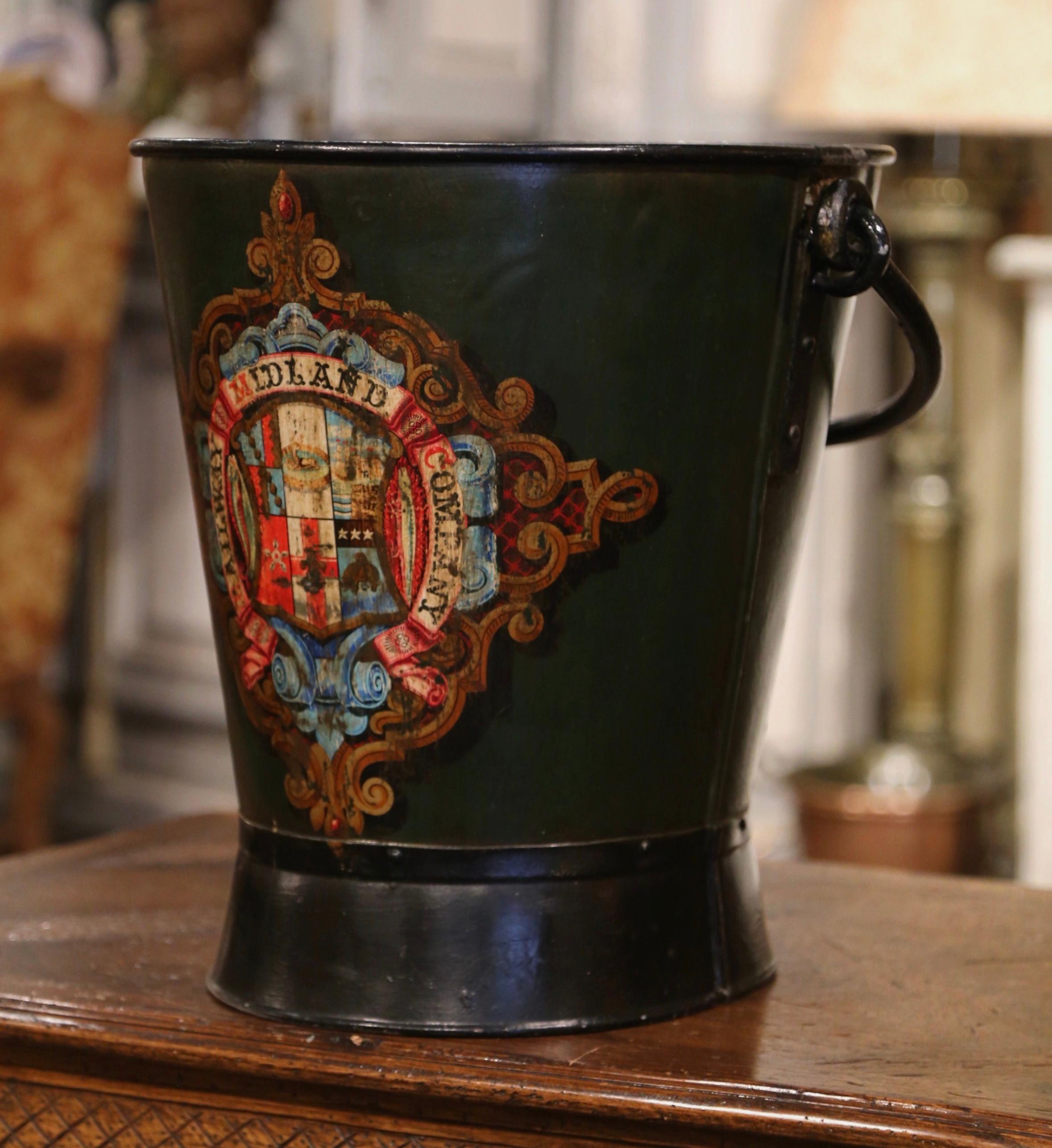 Place this large antique stand at your front door or in your mudroom to collect umbrellas, canes or other accessories. Created in England, circa 1890, the iron bucket with top and side handles, is decorated with a colorful crest and the Motto