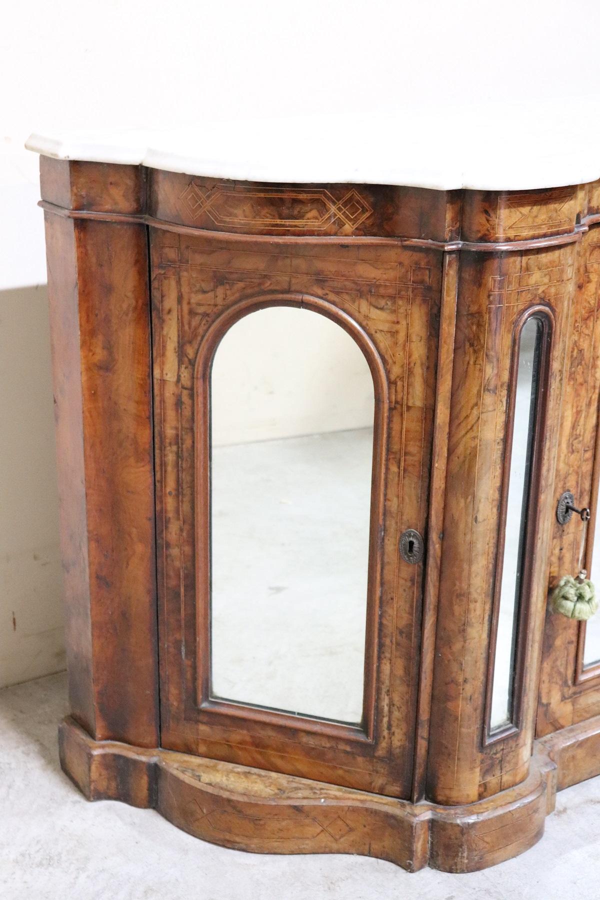 Antique English buffet 1850s in walnut inlaid wood. Particular and elegant rounded shape on the front and an elegant white marble top. On the front three doors with mirror. Ample useful internal space. This piece of furniture brings together all the