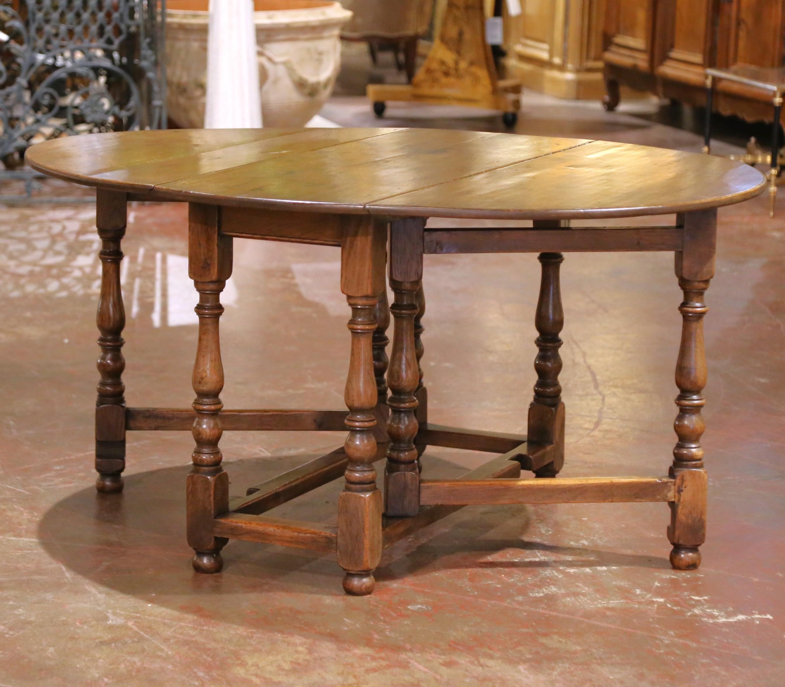 Crafted in England circa 1860, this versatile oak gate leg table is designed in the Jacobean Revival style, characterized by bold baluster-turned legs, a sturdy box stretcher base, and a functional drop-leaf form. The classic gateleg mechanism