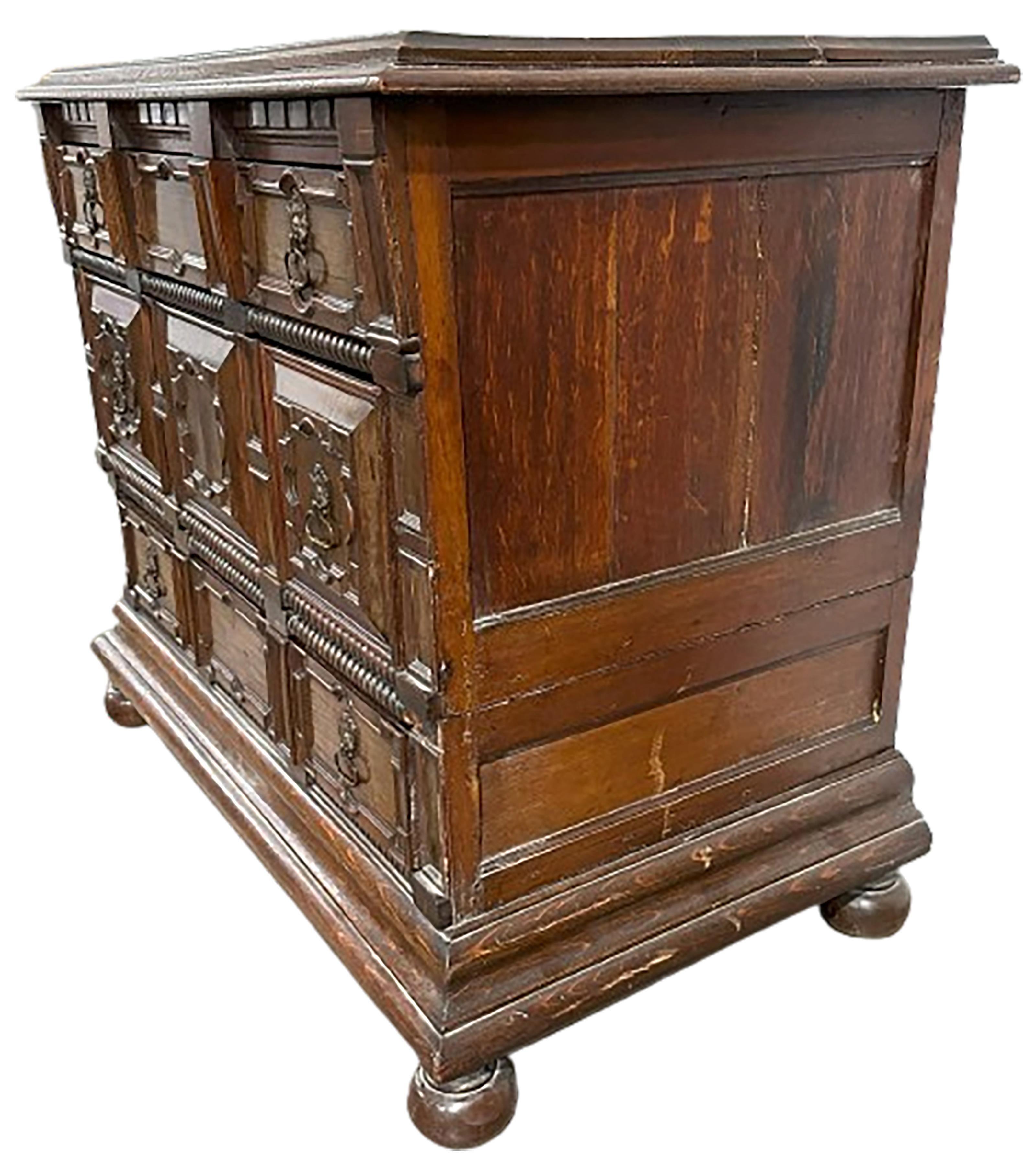 A handsome 19th century English Jacobean style chest of drawers. Finely carved cabinet drawers with brass handles with small gargoyle faces that open up three cabinets. Raised on cannonball feet. Divides up into two parts. Center and cabinet doors