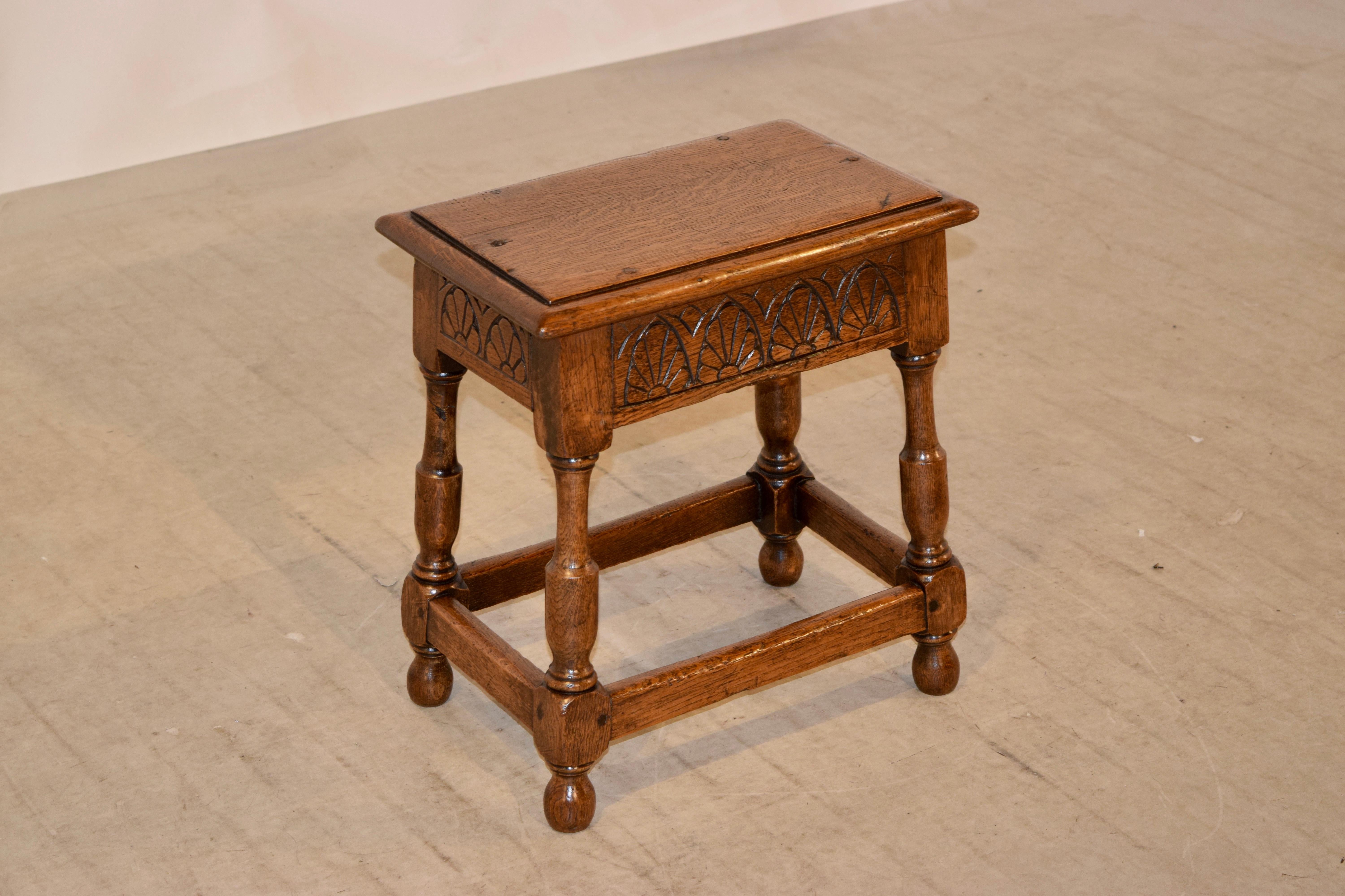 19th century English oak joint stool with a beveled edge around the top following down to hand carved aprons on all four sides for easy placement in any room. The legs are hand turned and splayed and are joined by simple stretchers. Supported on