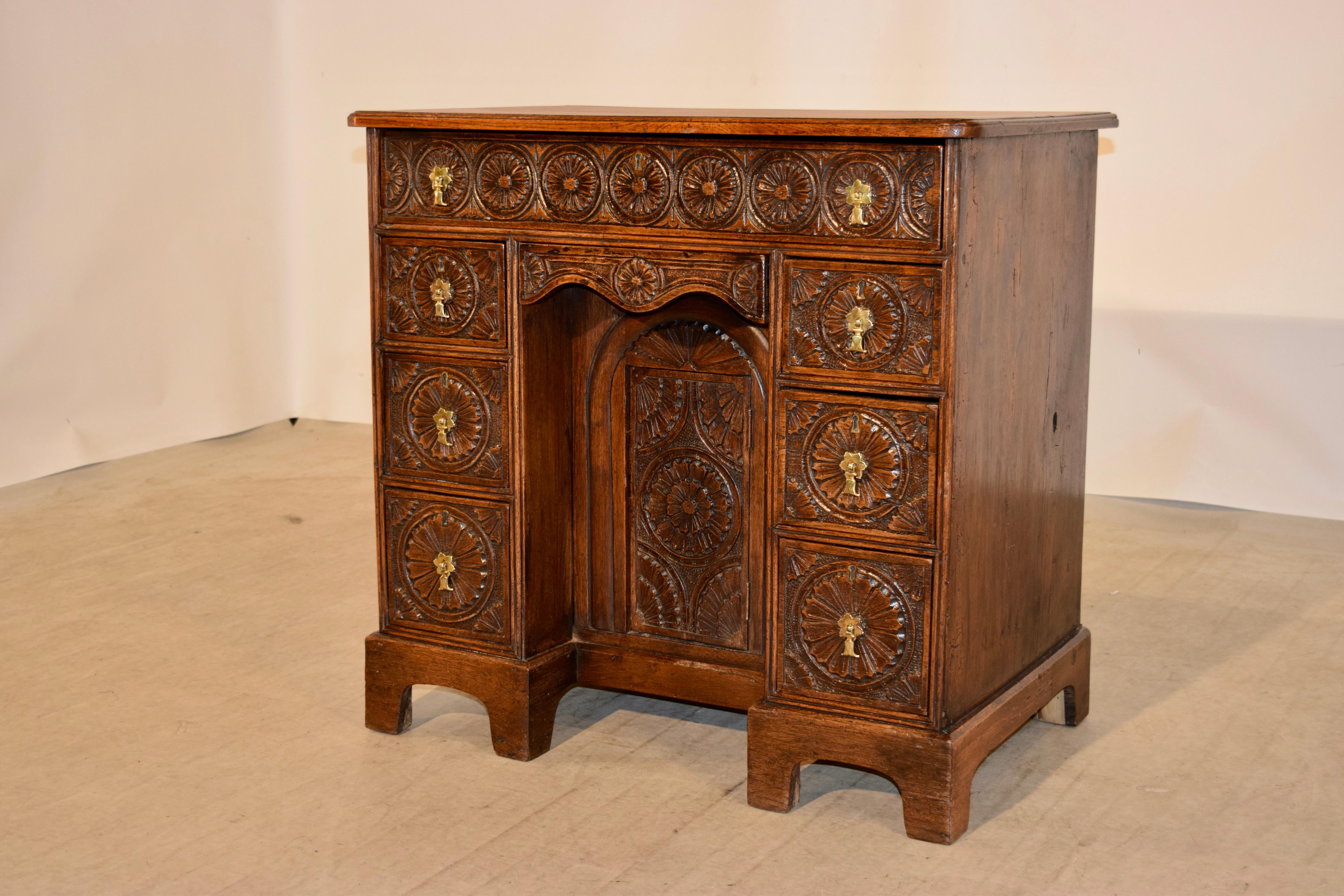 19th century English knee hole desk made from oak with a beveled edge around the top following down to a single drawer over two banks of three drawers each flanking a central door which opens to reveal storage. All of the drawer fronts and door are