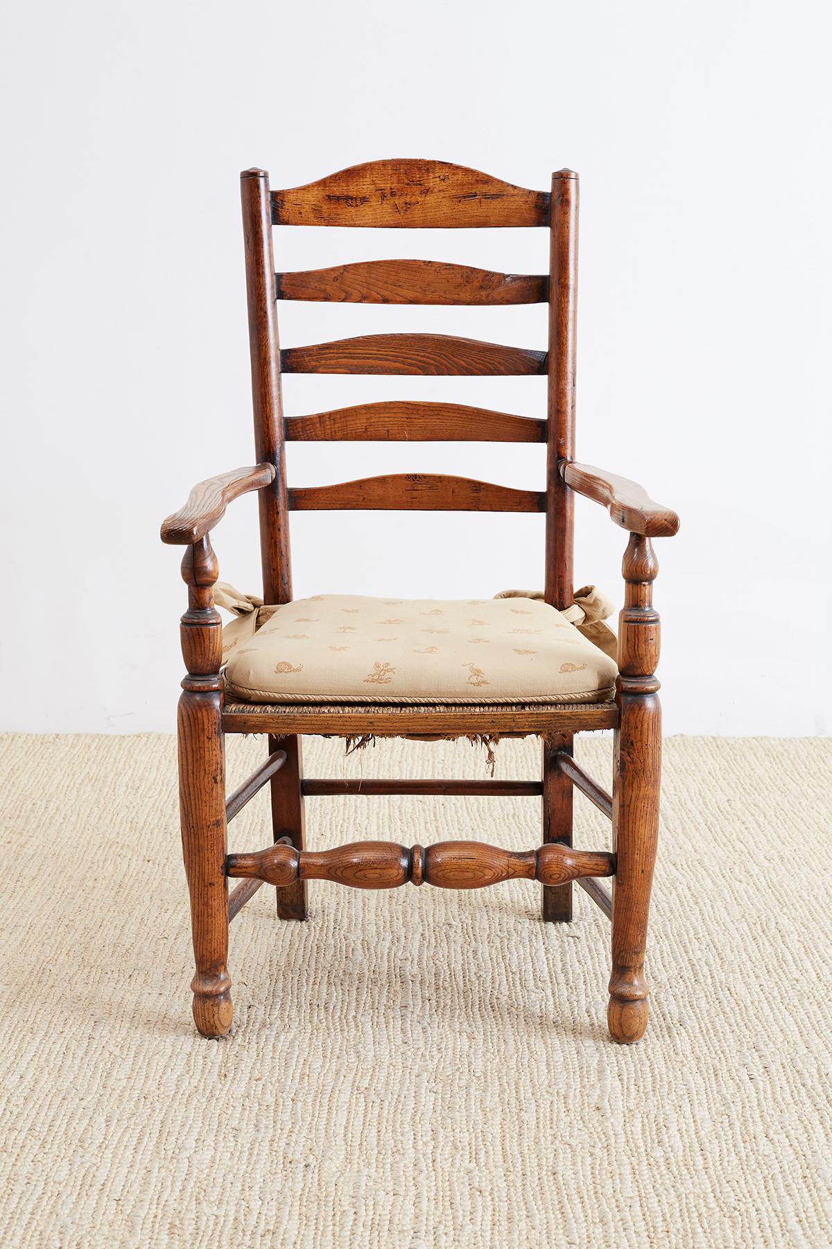 Large 19th century English carved oak armchair featuring a ladder back design and a rush seat. Sits on massive turned legs with box stretching. Wide elbow chair arms and a warm, rich patina on the vintage wood. From the Pebble Beach, California