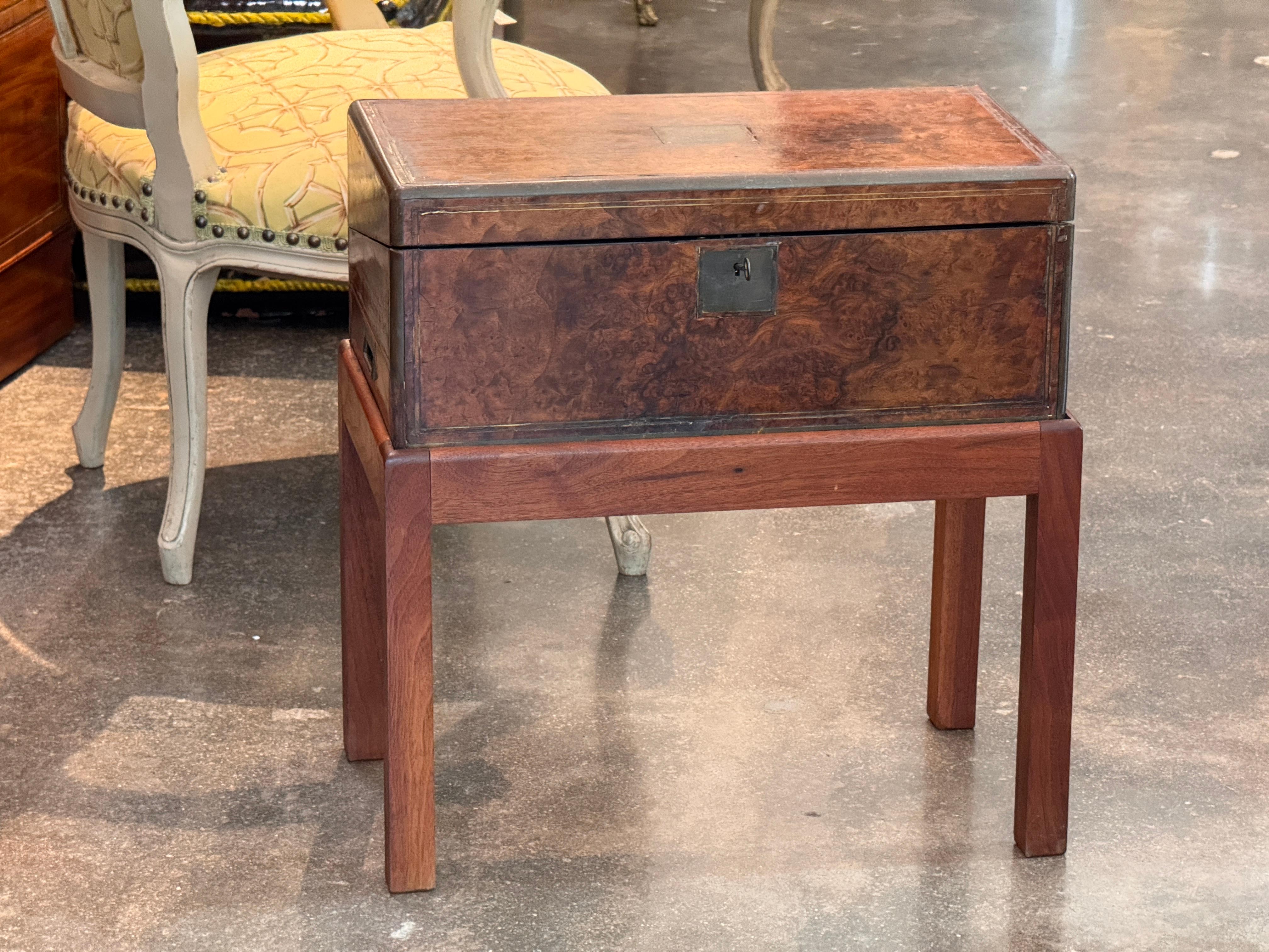 A 19th century English lap desk presented on a later custom stand. The burl veneer case is mounted with brass edging and fitted with a lock and recessed brass hardware. The hinged top opens to reveal a fitted interior with compartments for writing