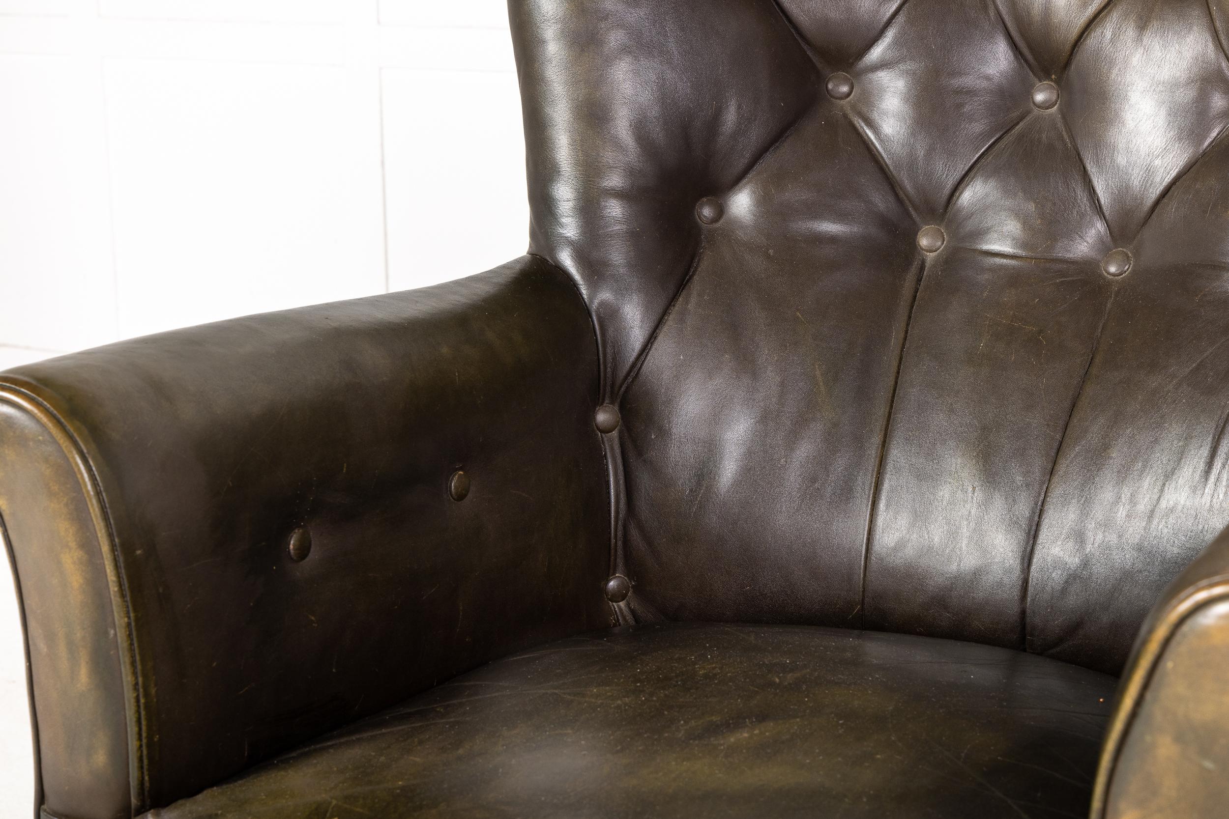A handsome, large scale 19th century English leather armchair having a wide button back with shallow wings and deep seat. Lovely old leather upholstery and decorative brass studding on the back and side edges. Raised on turned tapered legs, capped