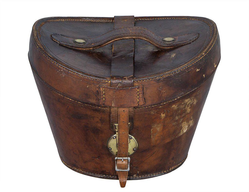 Gorgeous English leather hat box, designed specifically for a top hat. Accented with a front brass lock and front closing buckle. The interior is outfitted with worn red silk lining.