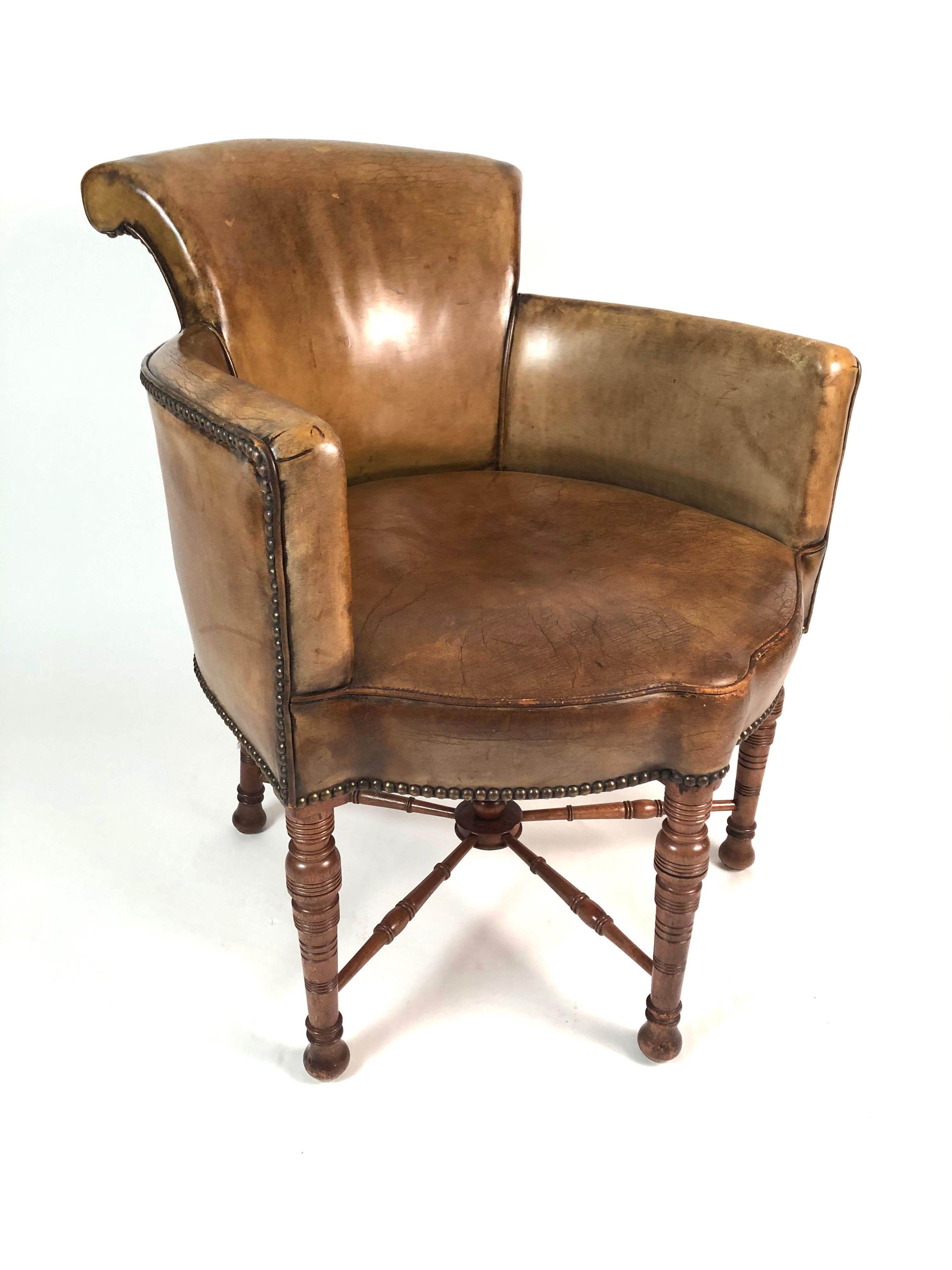 A 19th century English library chair, Aesthetic Movement period, upholstered in olive green leather, with scrolled back, curved arms and a shaped seat supported by four incised, ring- turned legs joined by cross stretchers, circa 1875. Comfortable