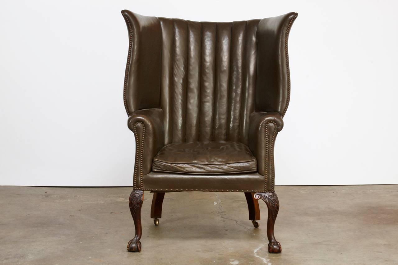 Distinctive 19th century English leather porters wingback chair. Features a mahogany hand-carved frame with a barrel back design. Finished in a deep, dark green color with brass nailhead trim accents. This rare wing chair was crafted with large