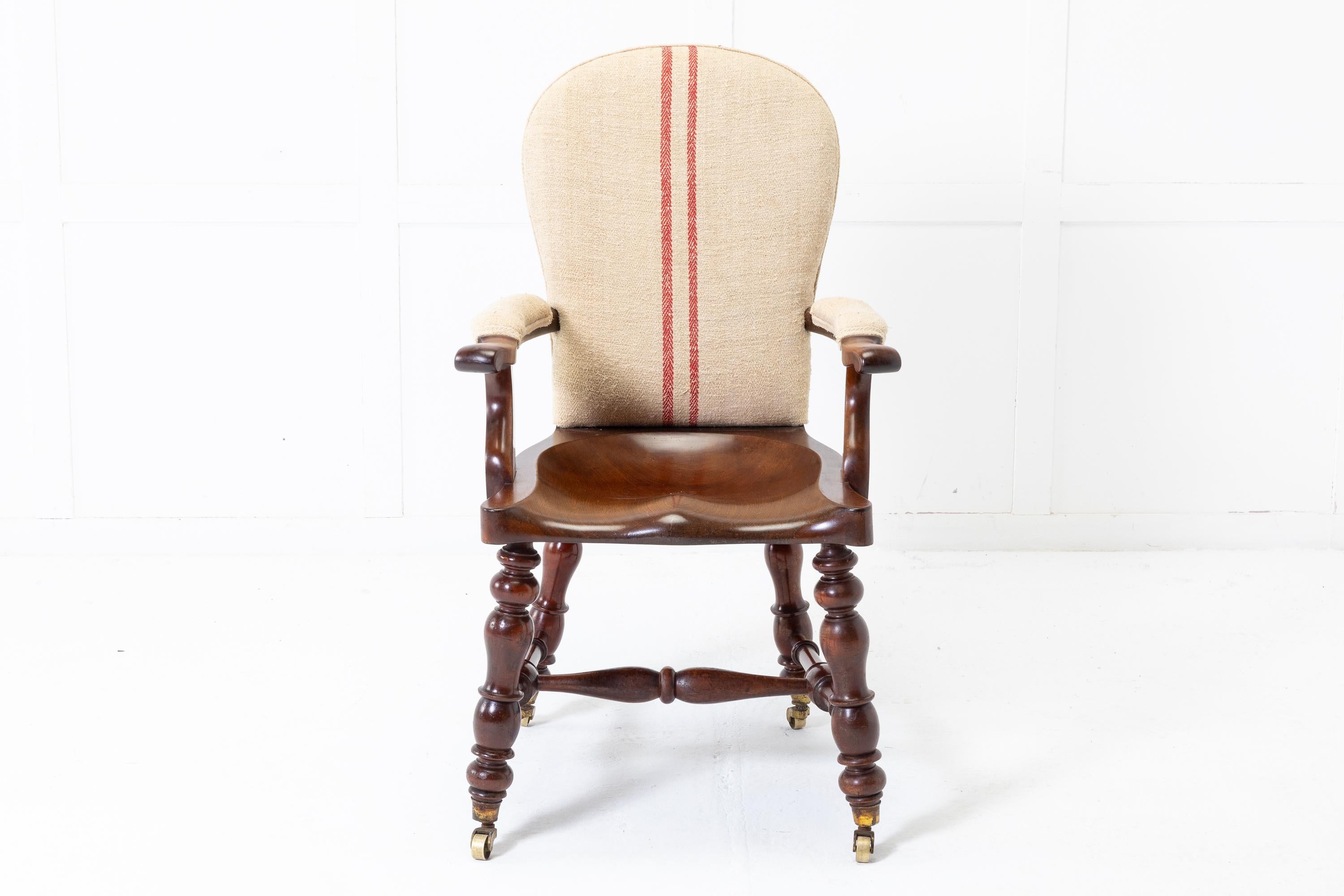 Substantial quality, heavy 19th Century English mahogany armchair with open arms and dished saddle seat. Having nicely turned legs and turned cross stretcher. Terminating in brass castors. Upholstered in old hemp fabric.

A very good chair!
