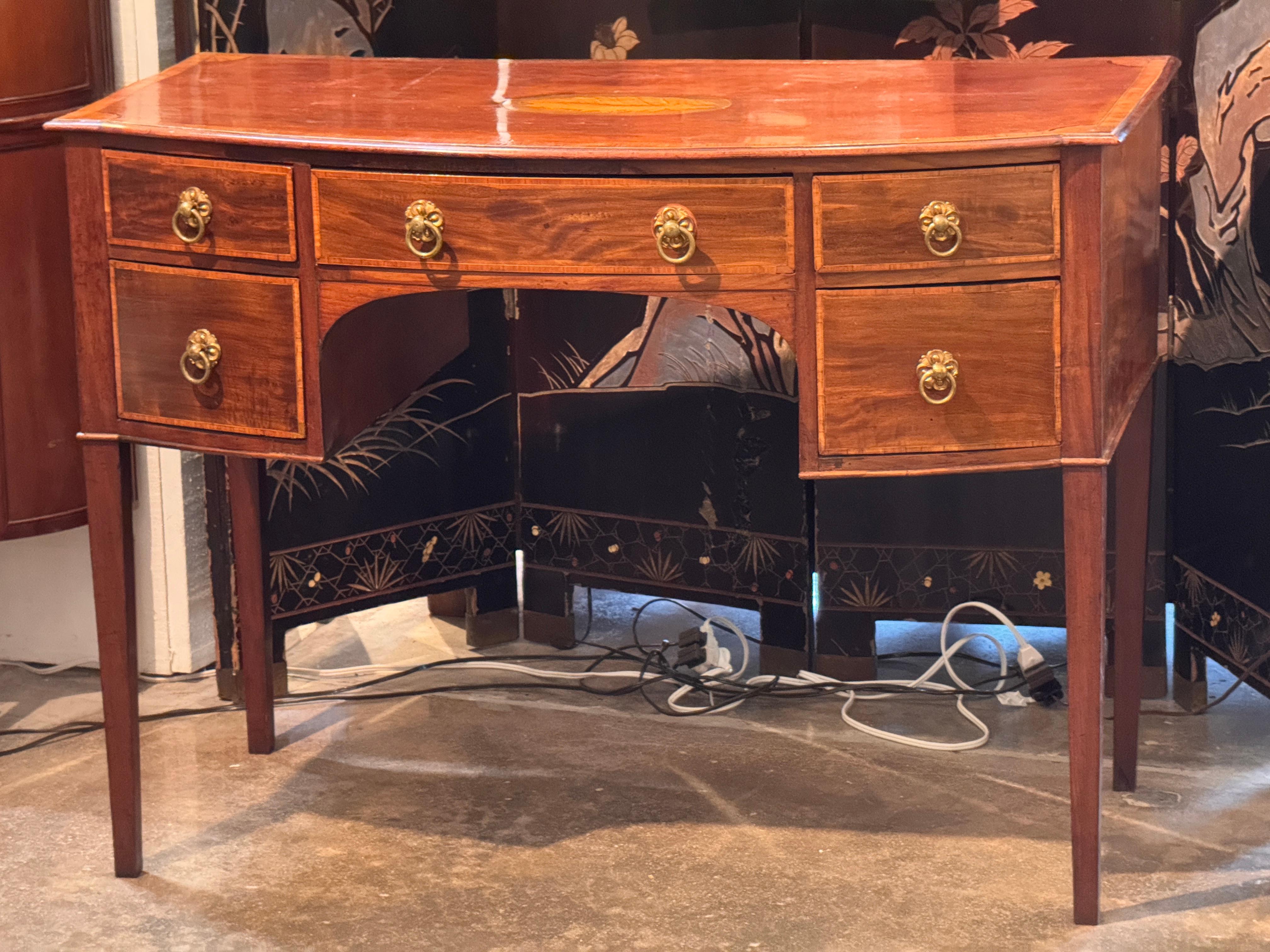 English mahogany brandy board featuring a shaped front, inlaid drawer banding, and fine stringing throughout. The top displays a central inlaid patera with ribbon motif and fan inlays at the corners. Drawers are fitted with brass lion’s head ring