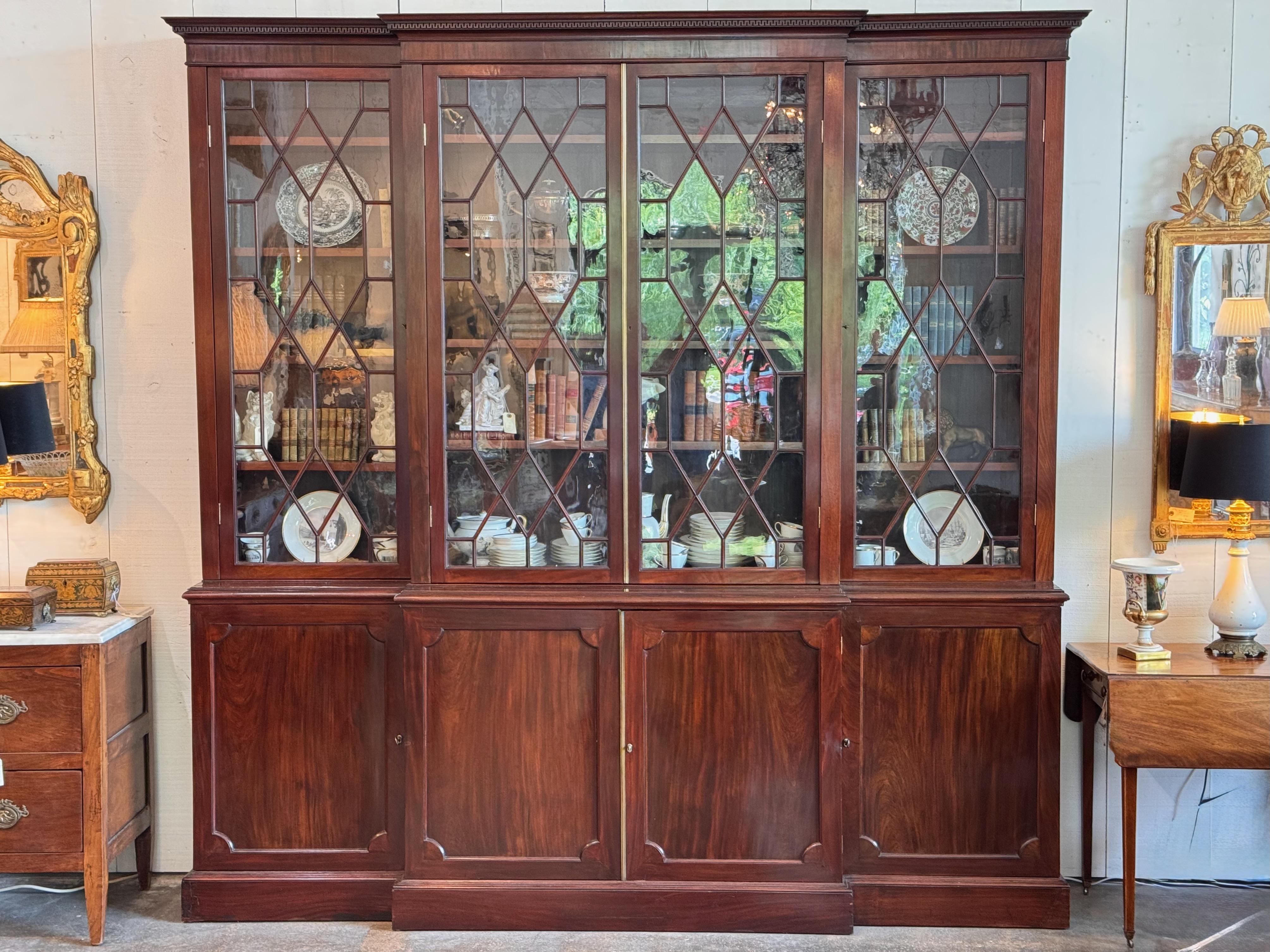 Substantial English breakfront cabinet in rich mahogany, 19th century. Upper section features diamond-mullioned glazed doors with shelving for books or display, while the lower cabinet offers paneled doors and interior storage with adjustable