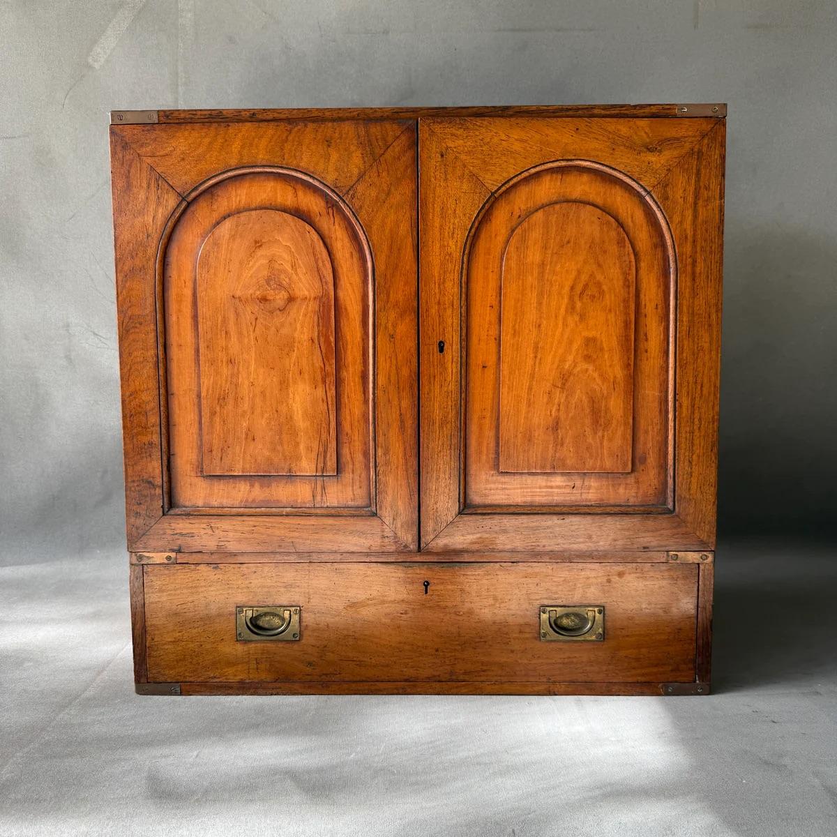 This 19th-century English mahogany tabletop campaign chest exudes a refined elegance with its rich warm hue and sophisticated brass hardware. It features two cabinet doors with beautifully carved arches, four spacious drawers within, and one large