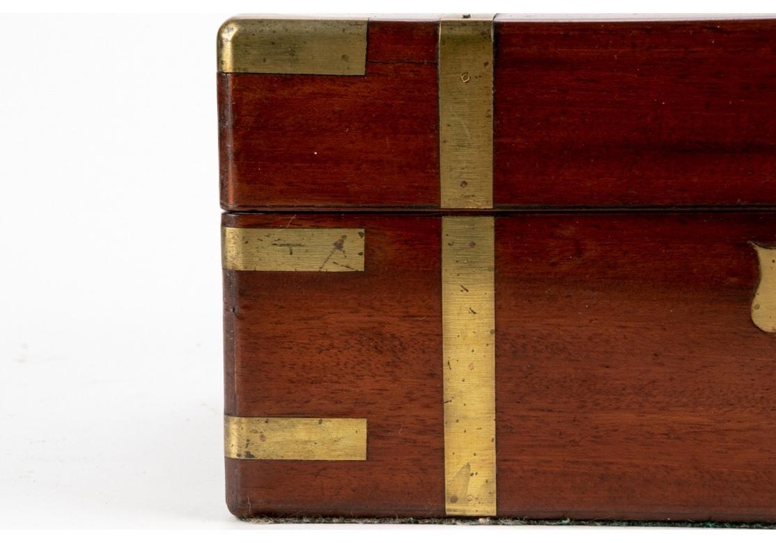 19th century English campaign travel lap desk. Rectangular form constructed out of mahogany with corner and banded brass accenting. Central inlaid brass crest. Top lifts open to reveal a velvet lined top that folds down to reveal a folio folder. The