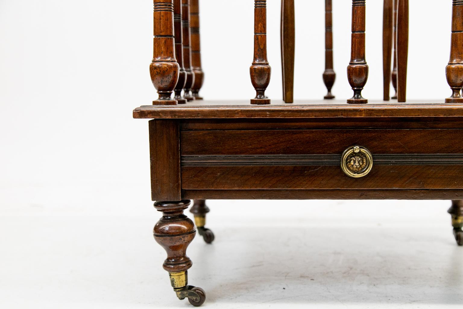 19th century English mahogany Canterbury, with three sections, turned spindle supports with finials on the corners. The legs are turned with original brass castors. It has one drawer.