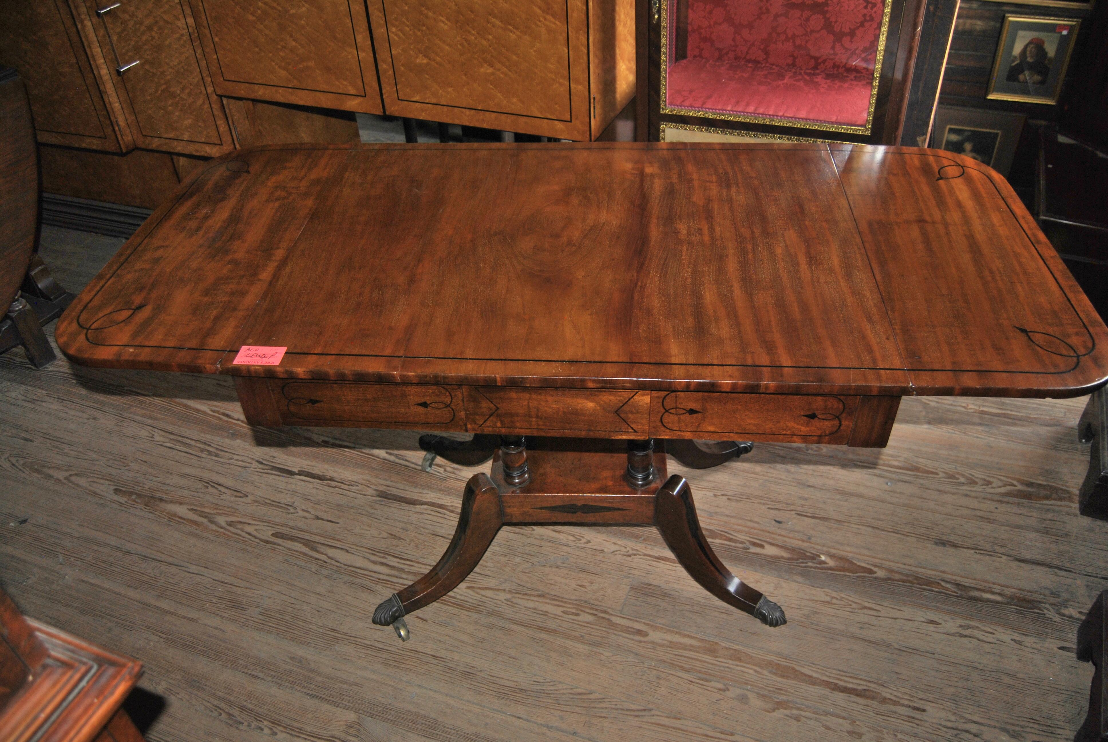 This is a solid mahogany drop leaf table made in England, circa 1825. The top, both leaves, the ring turnings on the pedestals, the platform base, the frame of the table and all 4 legs are inlayed with Ebony. There are 2 drawers to the front of the