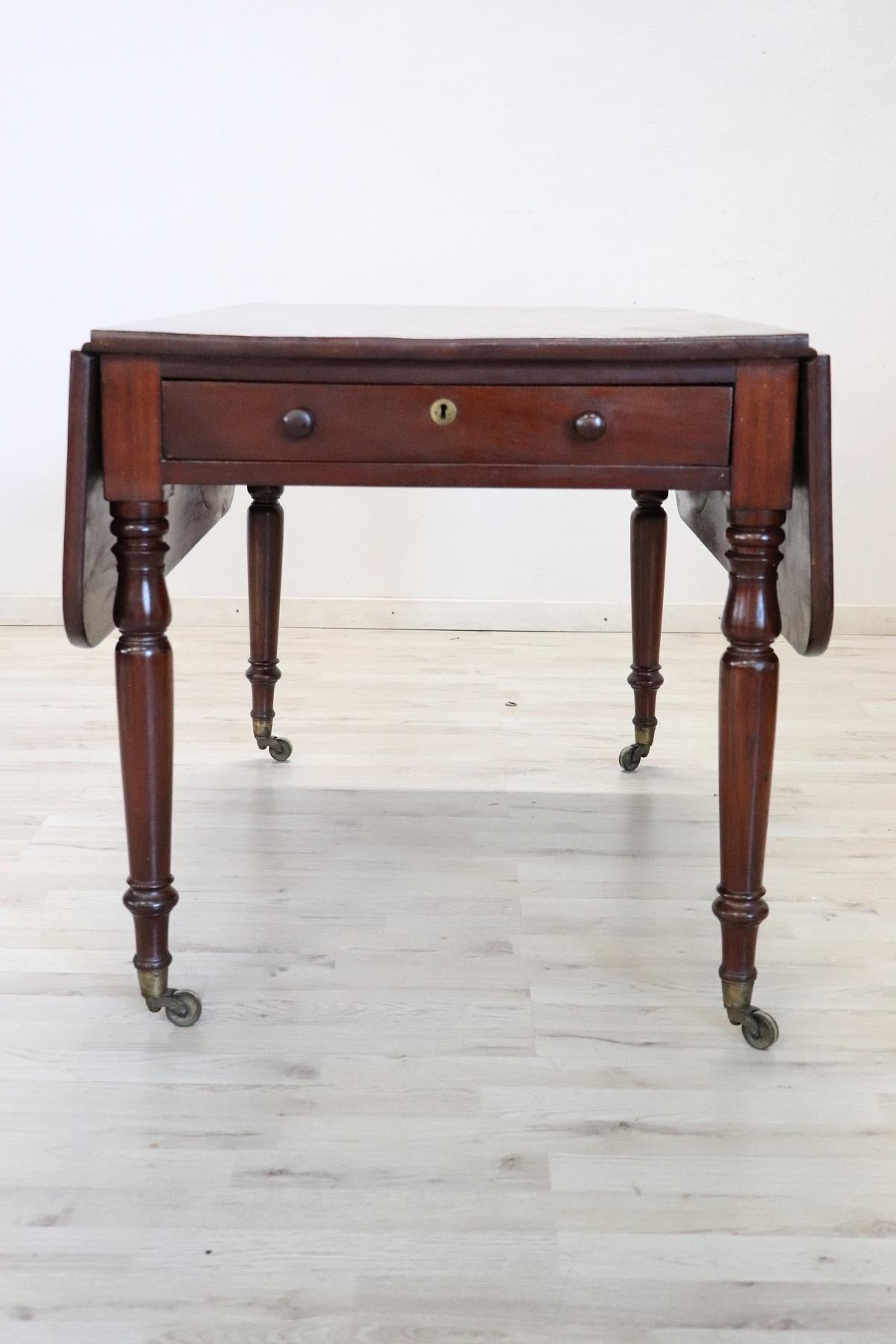 Elegant antique English drop-leaf table. The table is made of solid mahogany wood. Important turned legs. One comfortable drawer on the front. At the foot of the wheels for comfortable movement. Perfect conditions and ready to be inserted into your