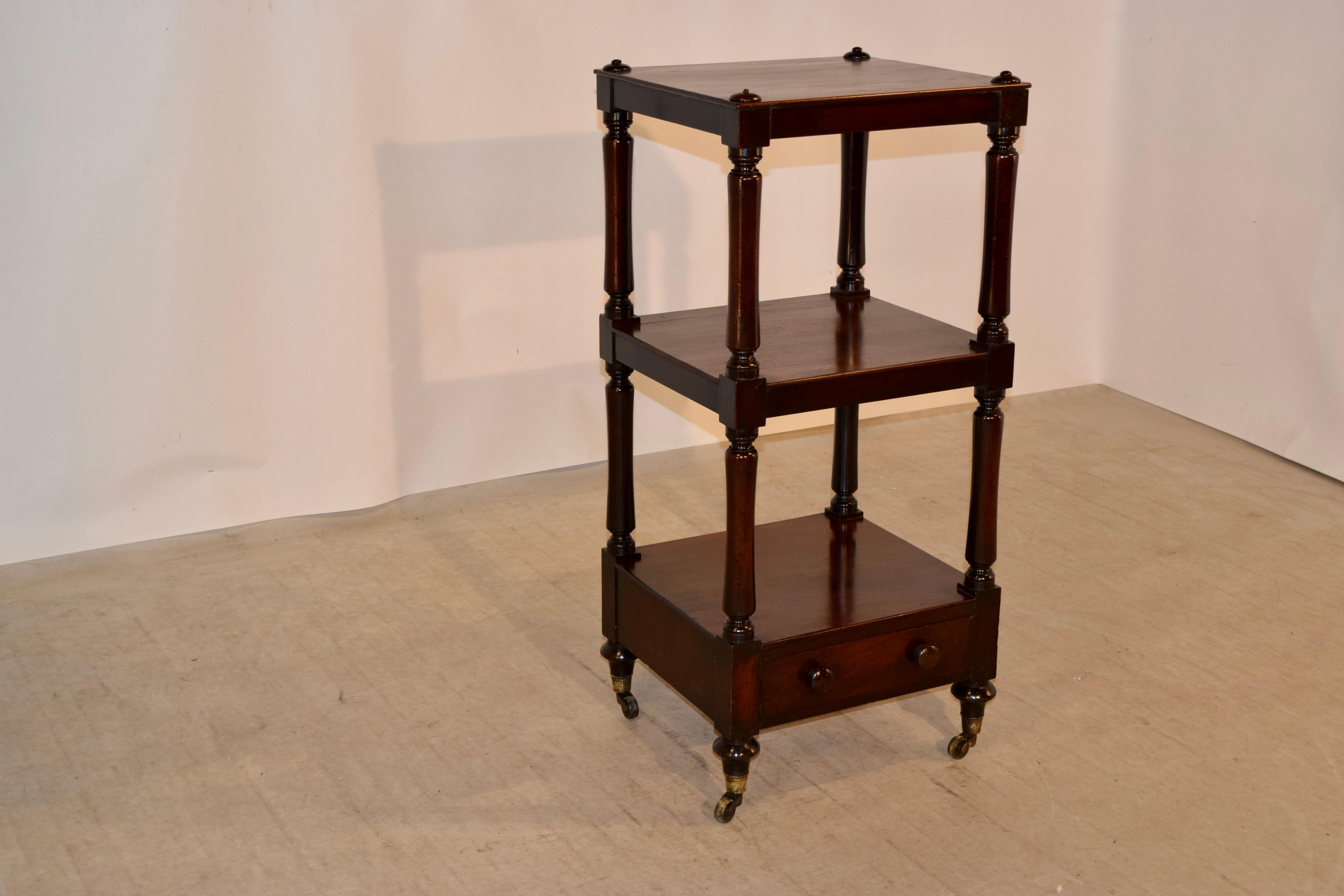 19th century English étagère made from mahogany. The top is decorated with hand turned caps over three shelves, separated by hand turned shelf supports. The lowest shelf contains a drawer and the piece is raised on hand cast brass casters.