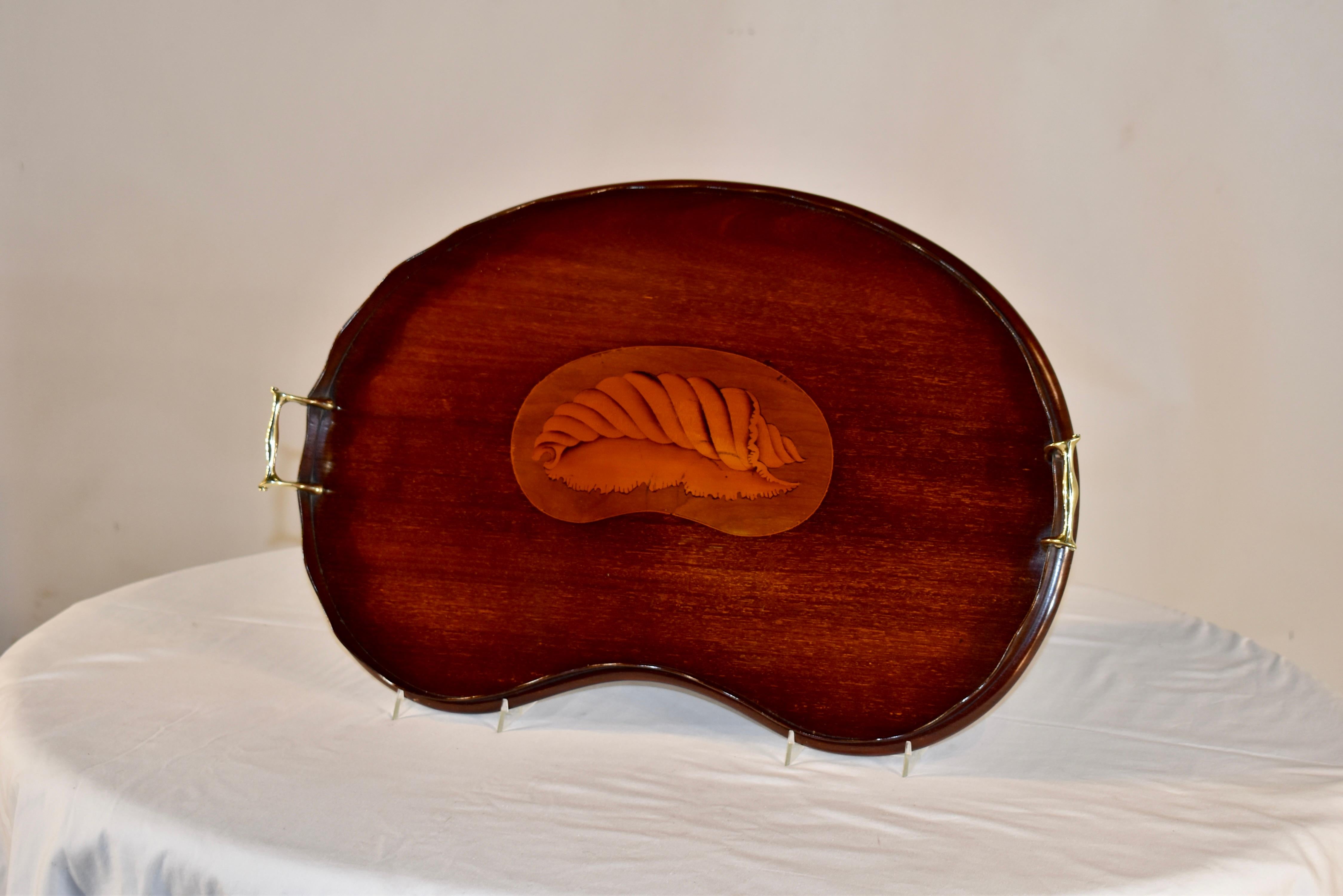 19th century mahogany tray from England with a lovely kidney shape. The tray is surrounded by a hand scalloped gallery and hand cast brass handles. In the center of the tray is an inlaid medallion with a wonderfully detailed shell in the center.