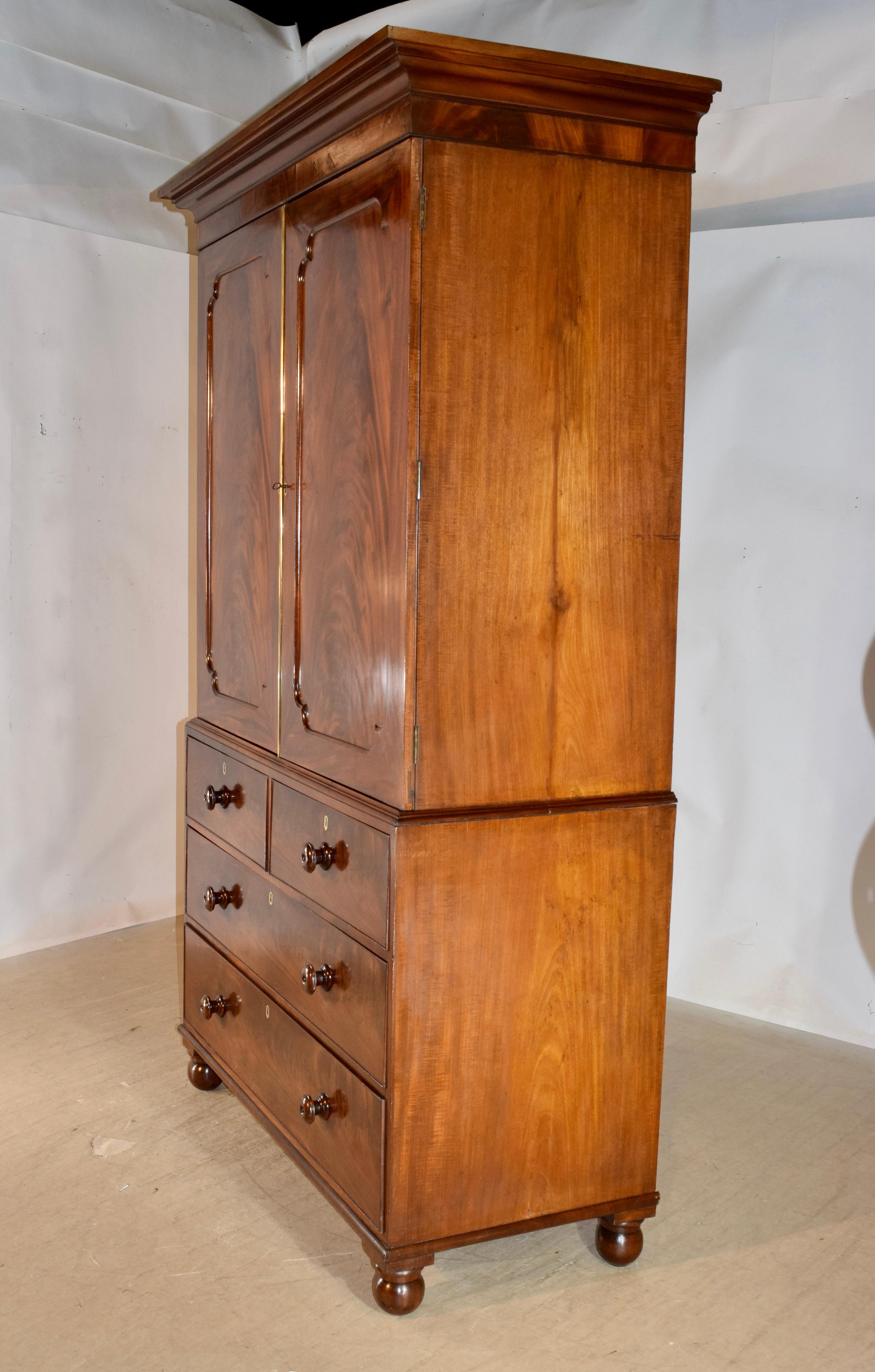 19th century mahogany linen press from England with a lovely crown on top over simple sides and two large paneled doors in the front with magnificent flame graining, which open to reveal the original mahogany slides. The door has brass molding on