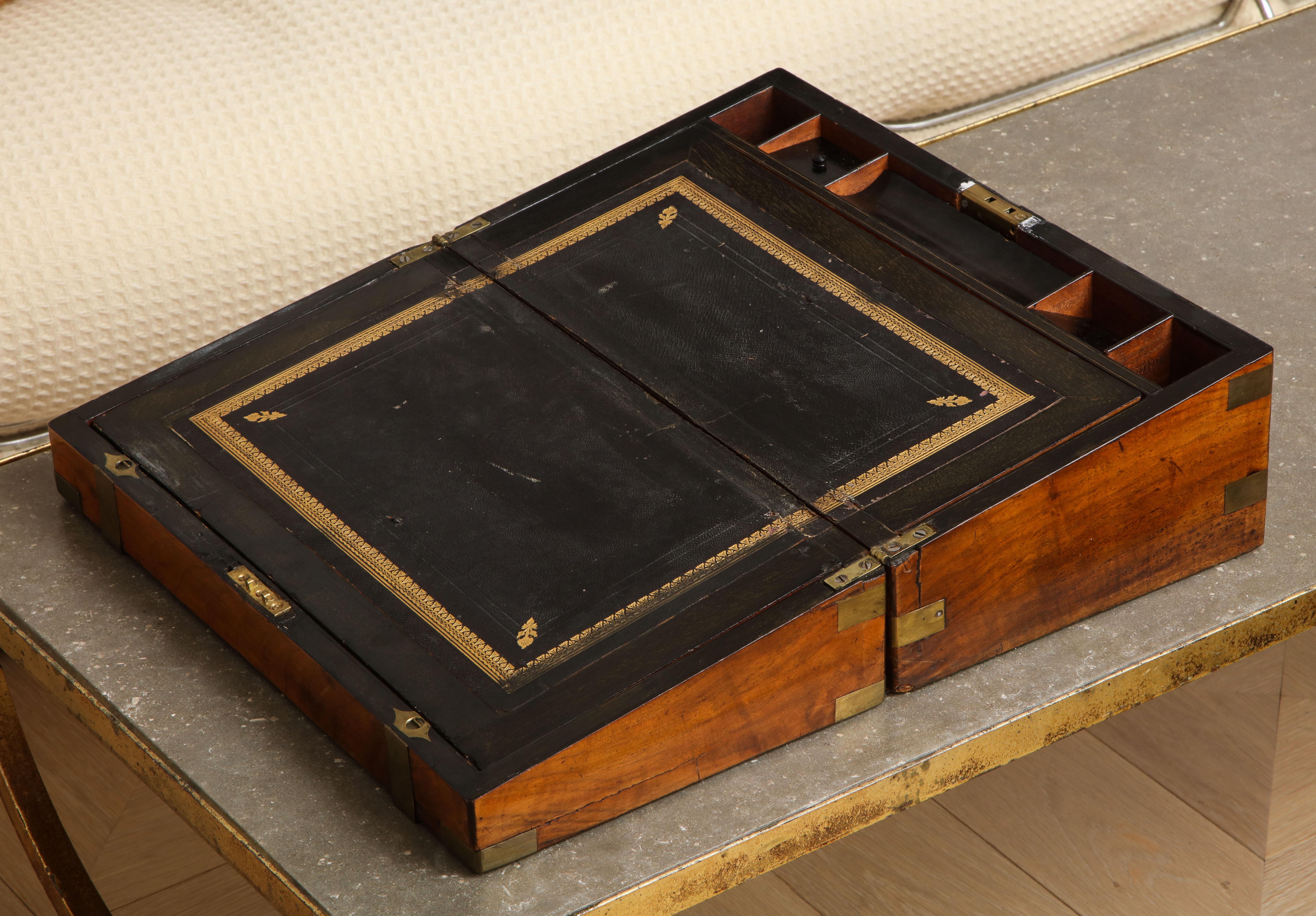 19th century English Campaign portable mahogany writing box with brass bound molded edges and brass banding. Black leather writing slope with gold edge details and the rear half opens for storage. Unmarked brass plate on top. 

When full open,